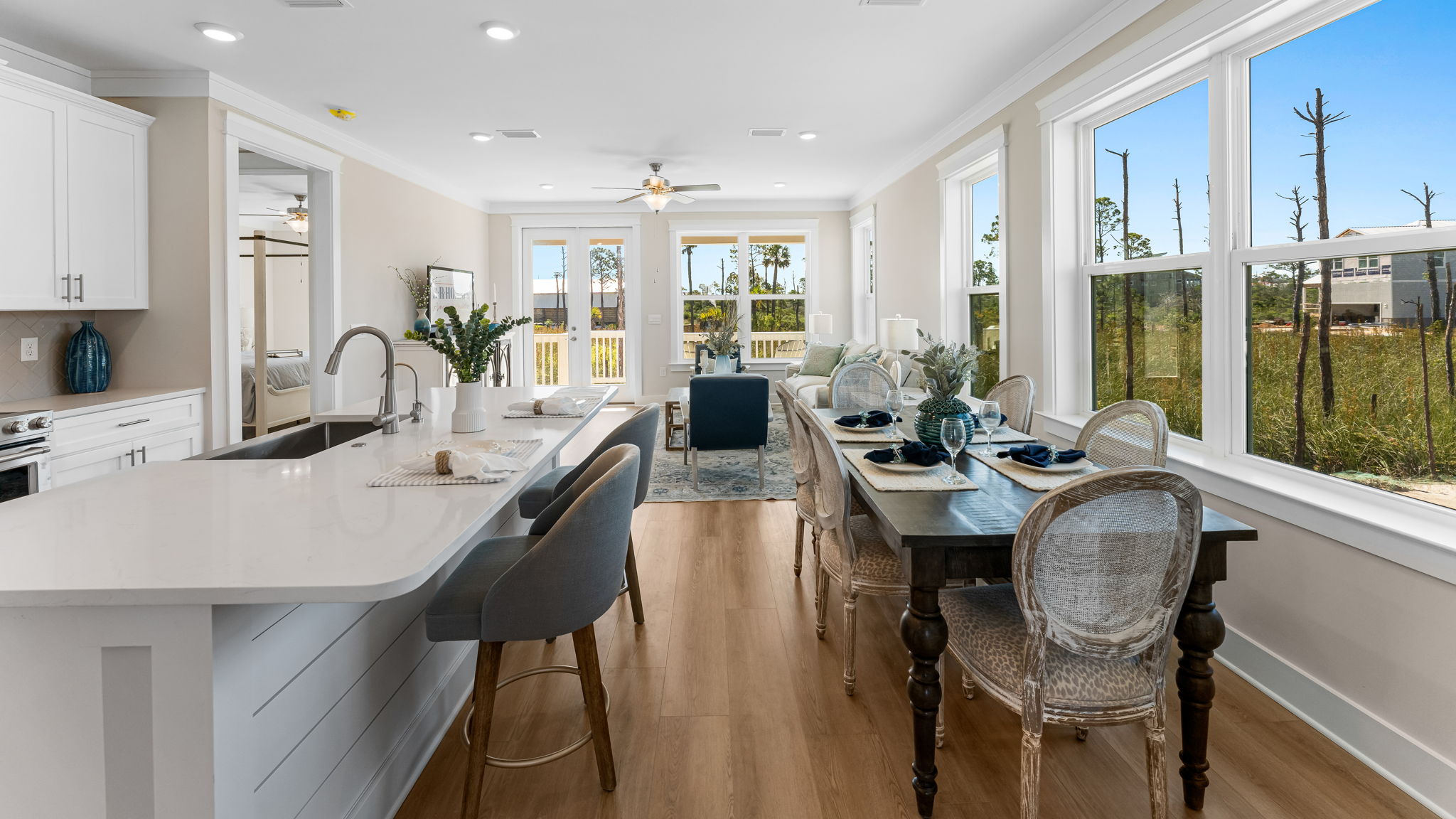 Kitchen island with dining area looking into open living room with large windows.