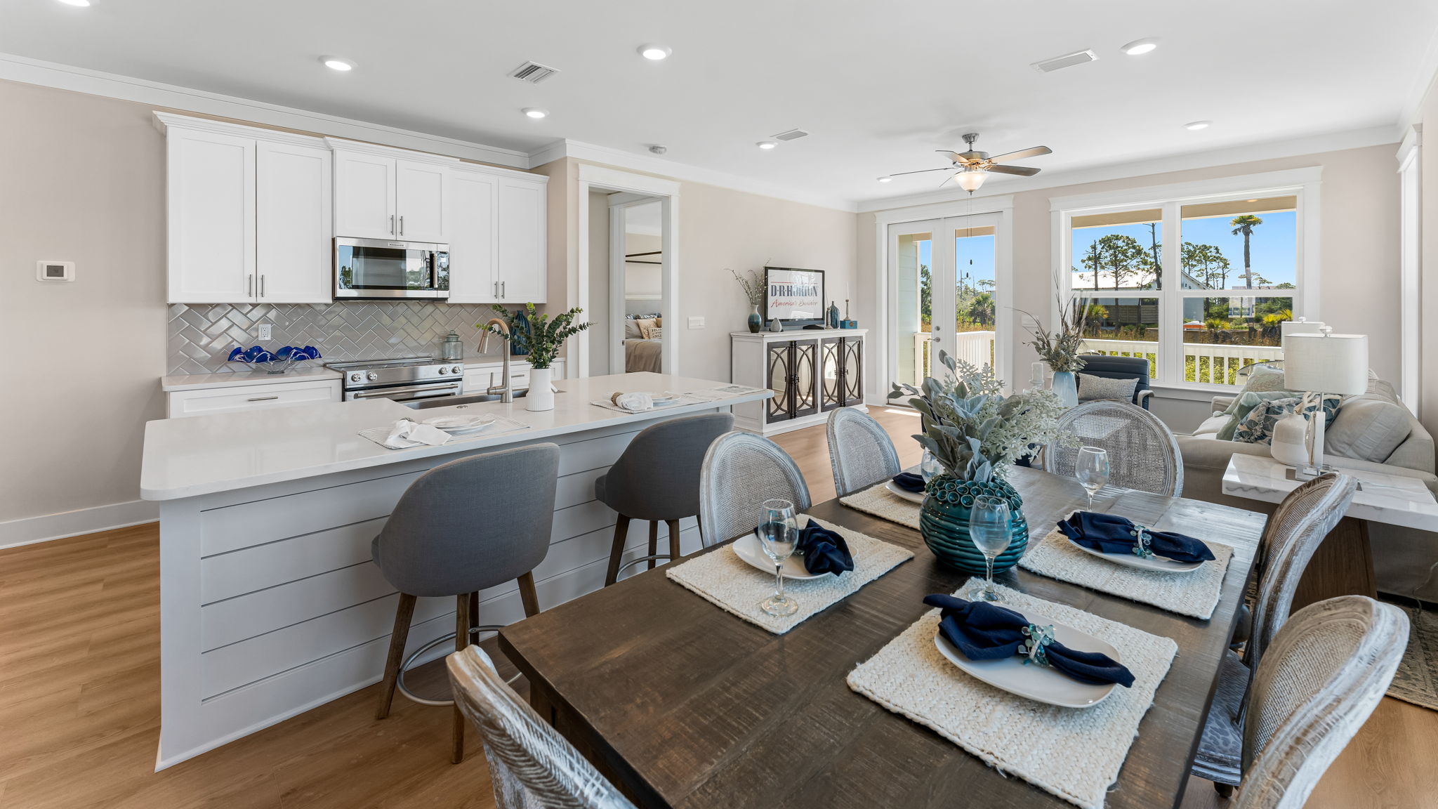 Kitchen island with dining area looking into open living room with large windows.