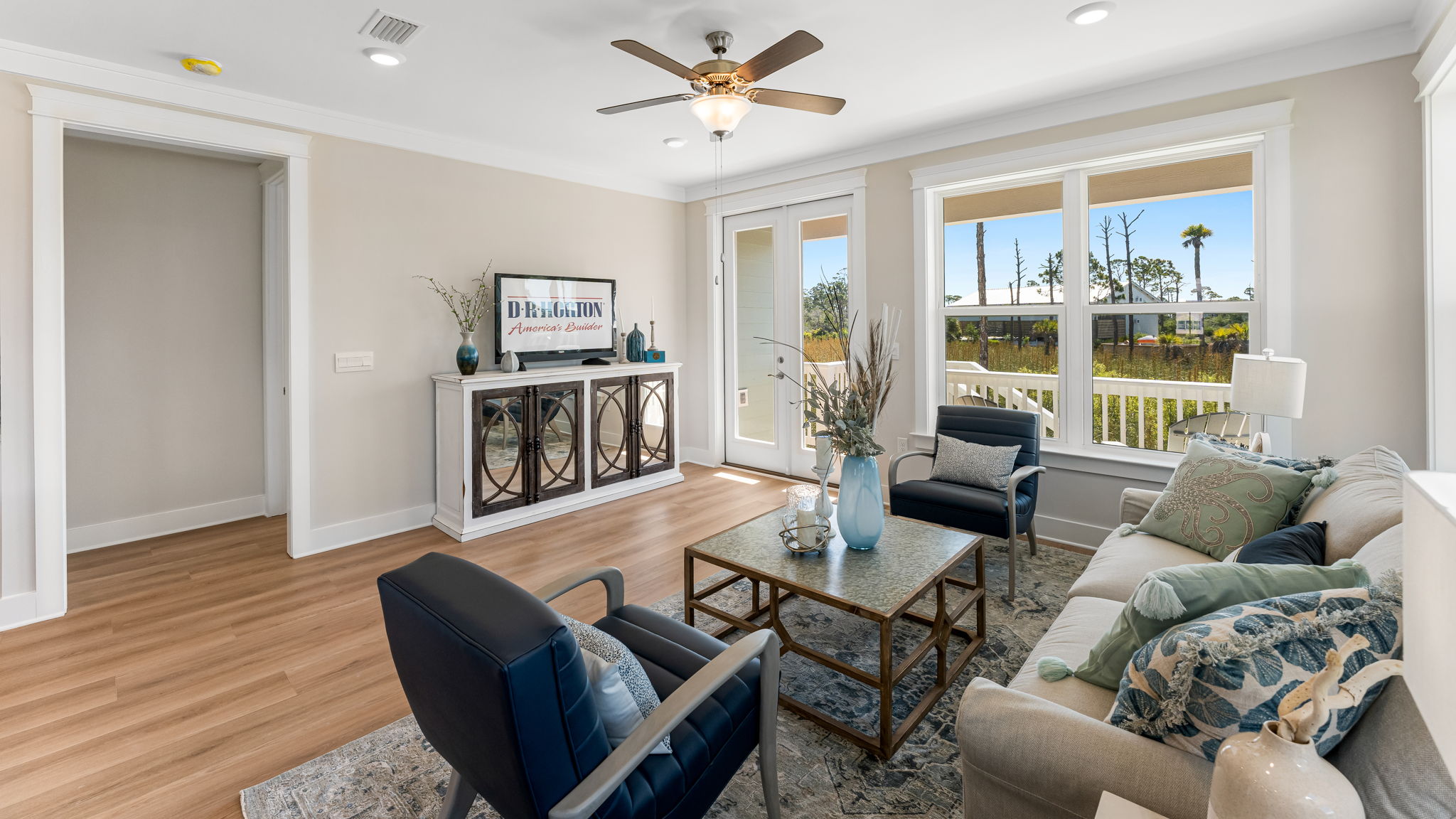 Open furnished living room with EVP flooring and ceiling fan and large windows and back door.