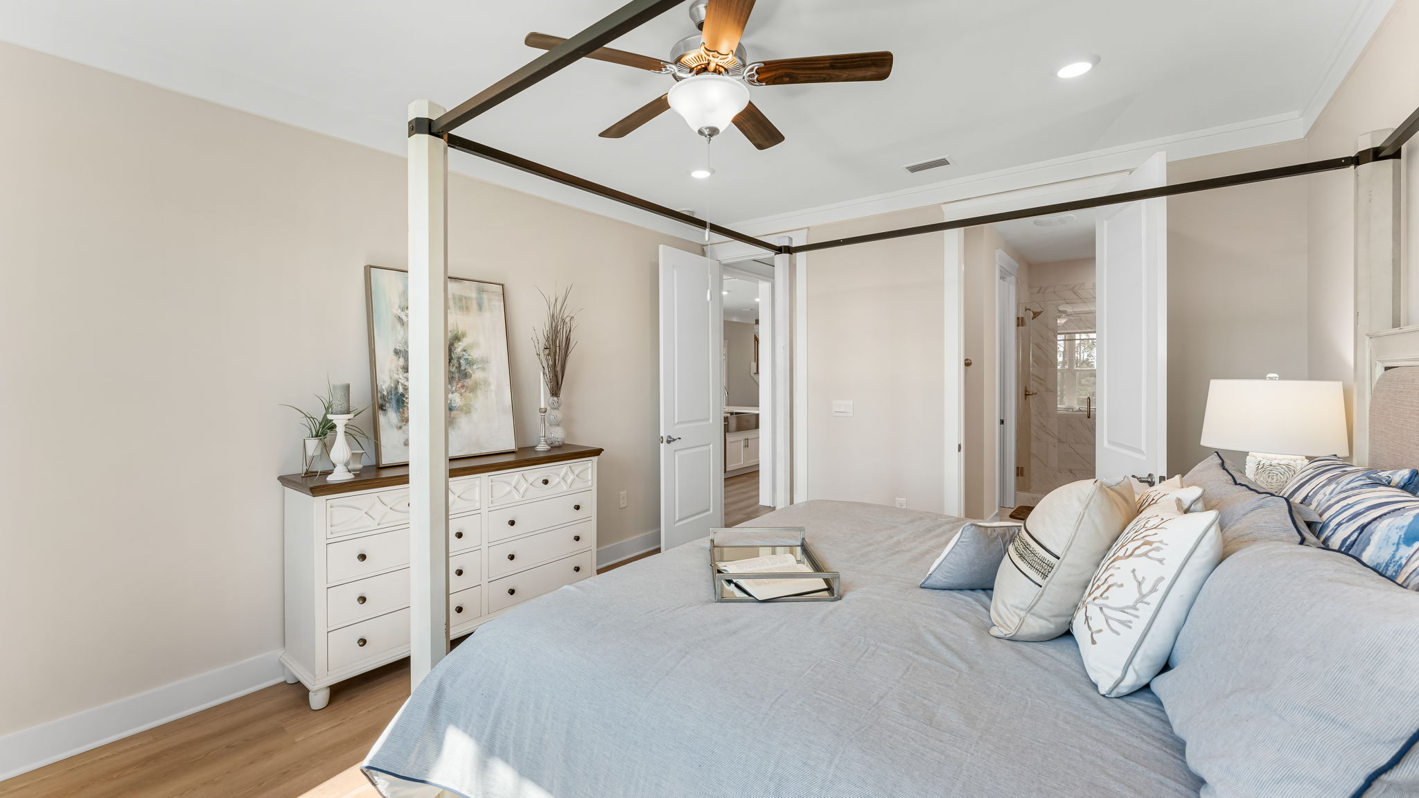 Furnished primary bedroom with EVP flooring and ceiling fan and bathroom entrance.