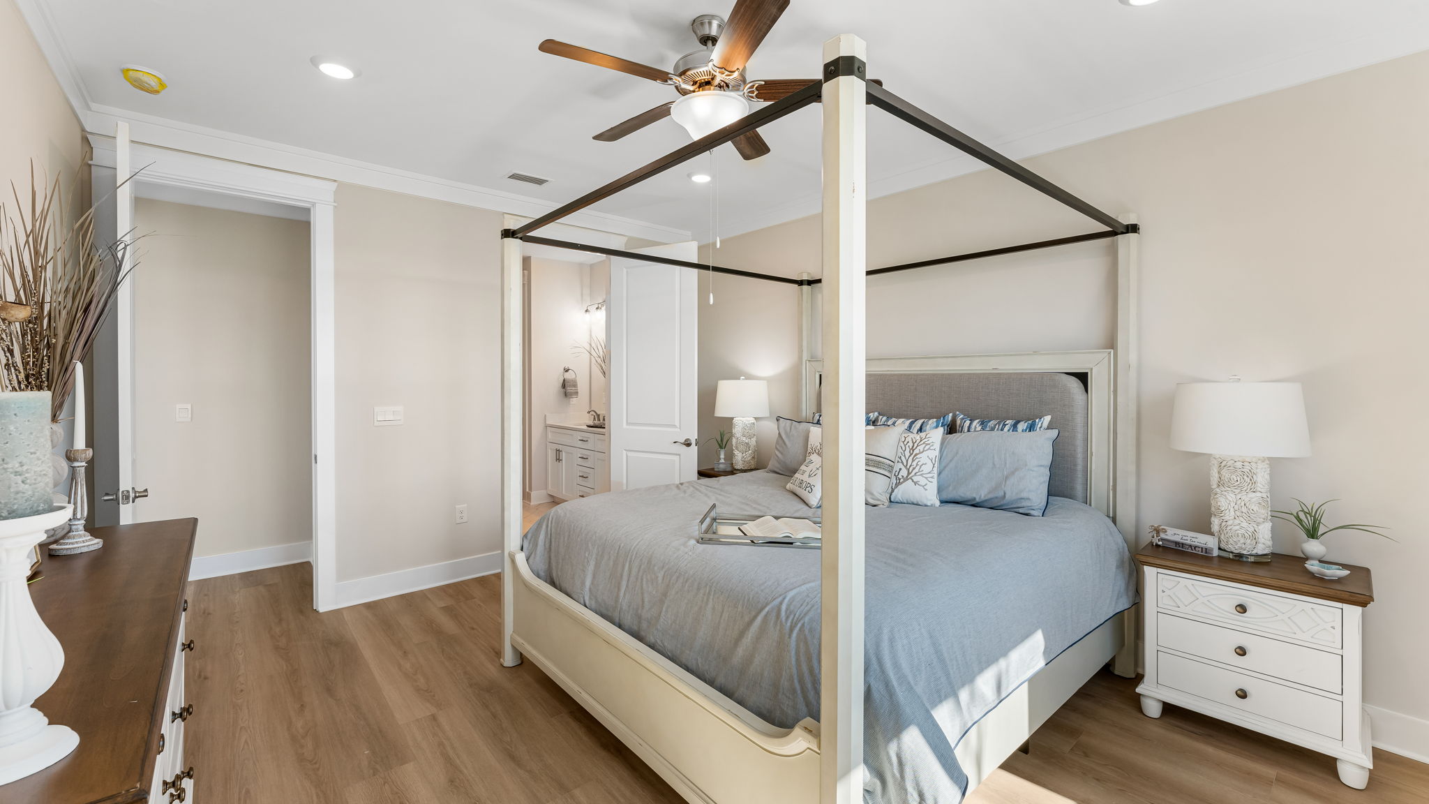 Furnished primary bedroom with EVP flooring and ceiling fan and bathroom entrance.