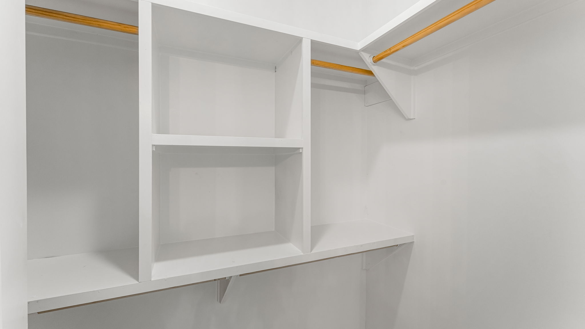 Primary bathroom closet with white shelving and wooden clothing rack.