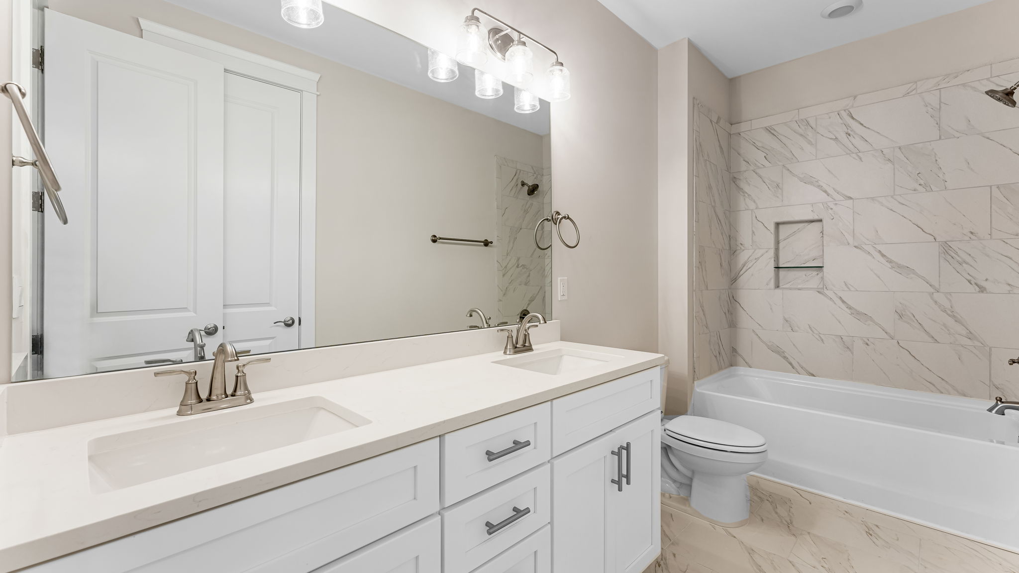 Bathroom with double vanity quartz countertops with white cabinets and Florentine tiled shower and tub combo.