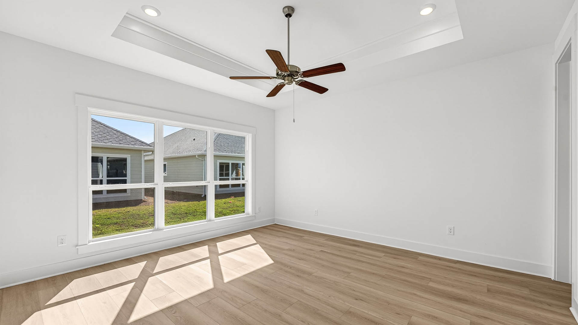 Primary bedroom with EVP flooring and Ceiling fan and tray ceilings and window.