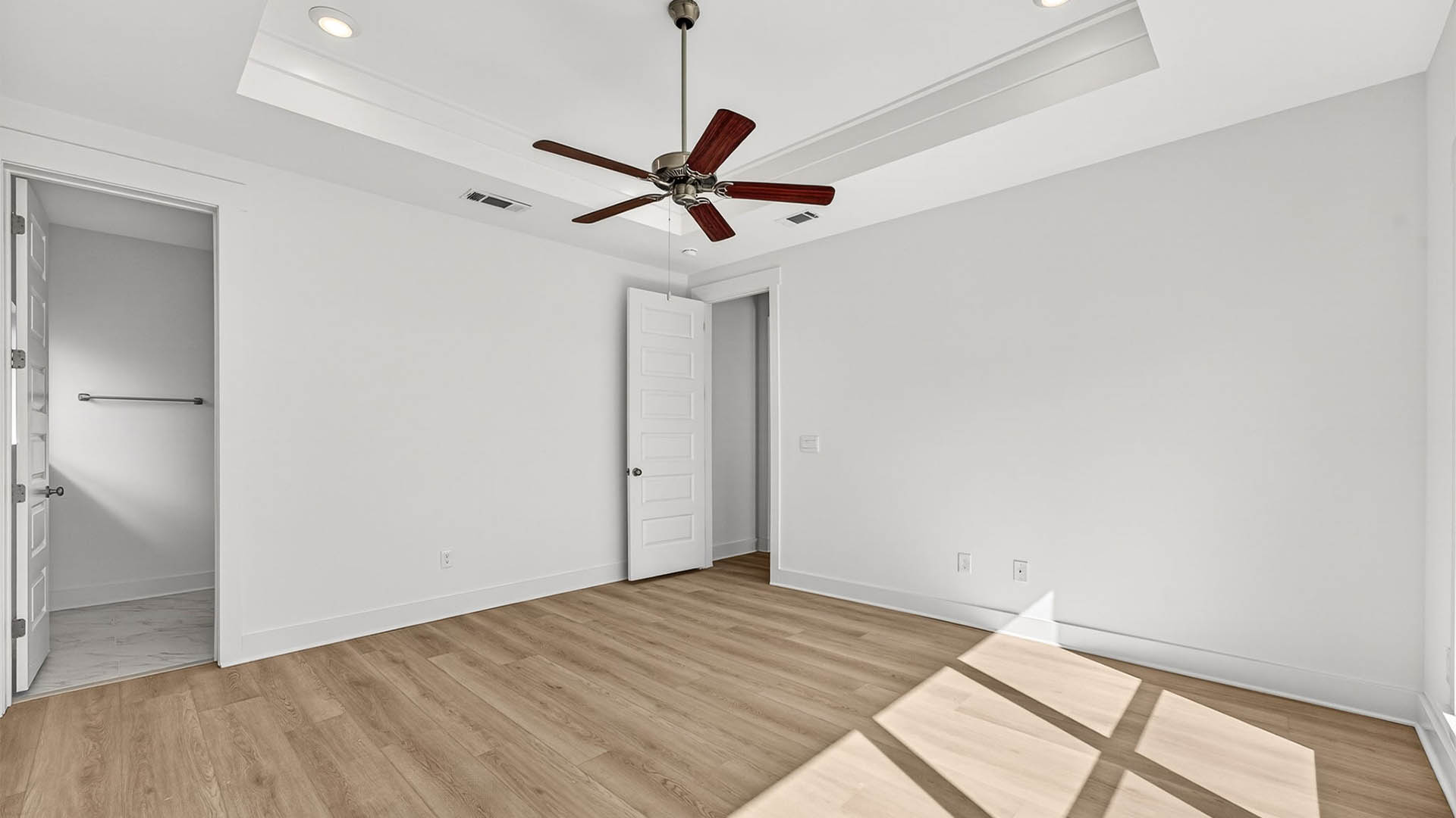 Primary bedroom with EVP flooring and Ceiling fan and tray ceilings and bathroom entrance.