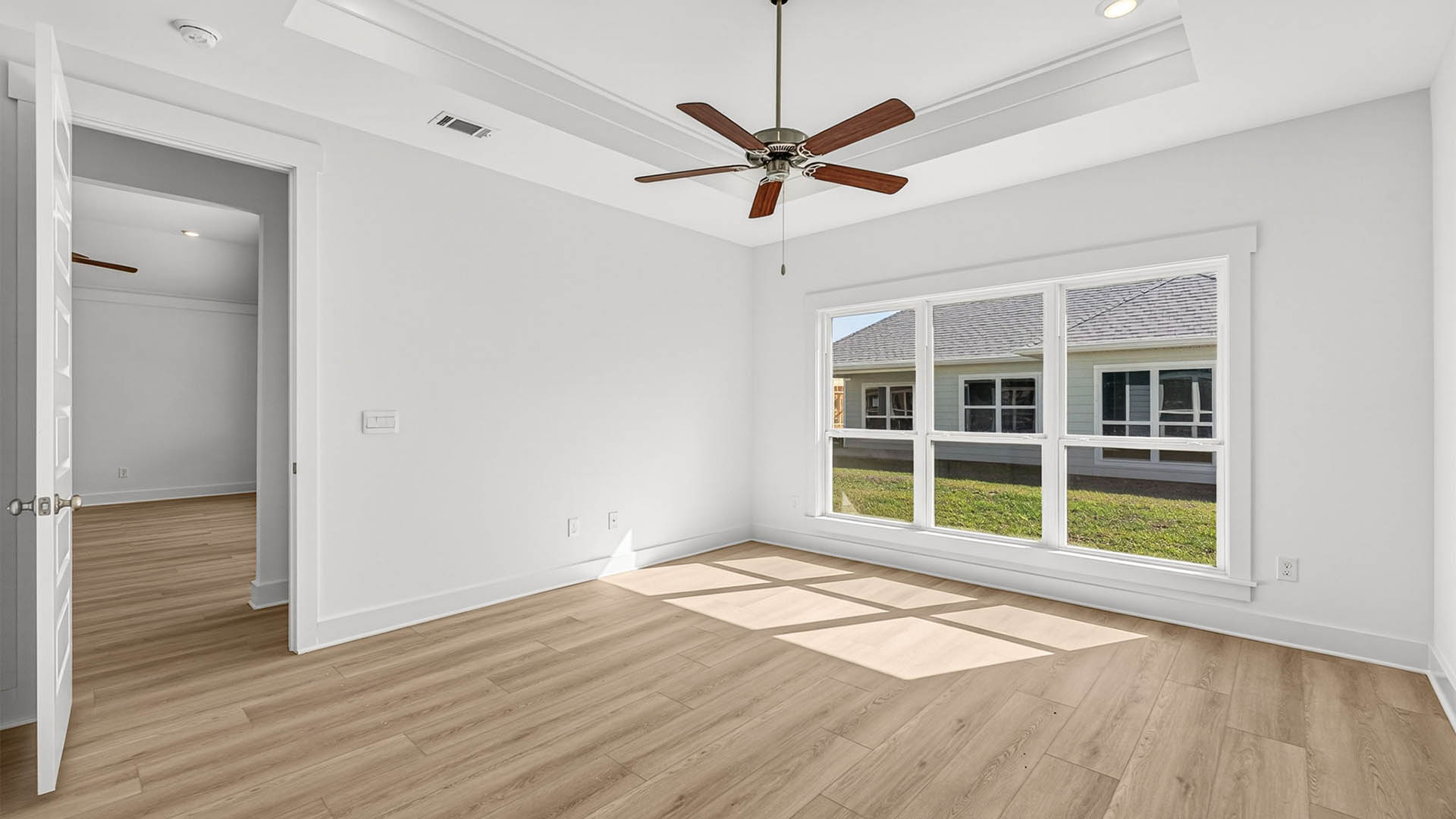 Primary bedroom with EVP flooring and Ceiling fan and tray ceilings and window.
