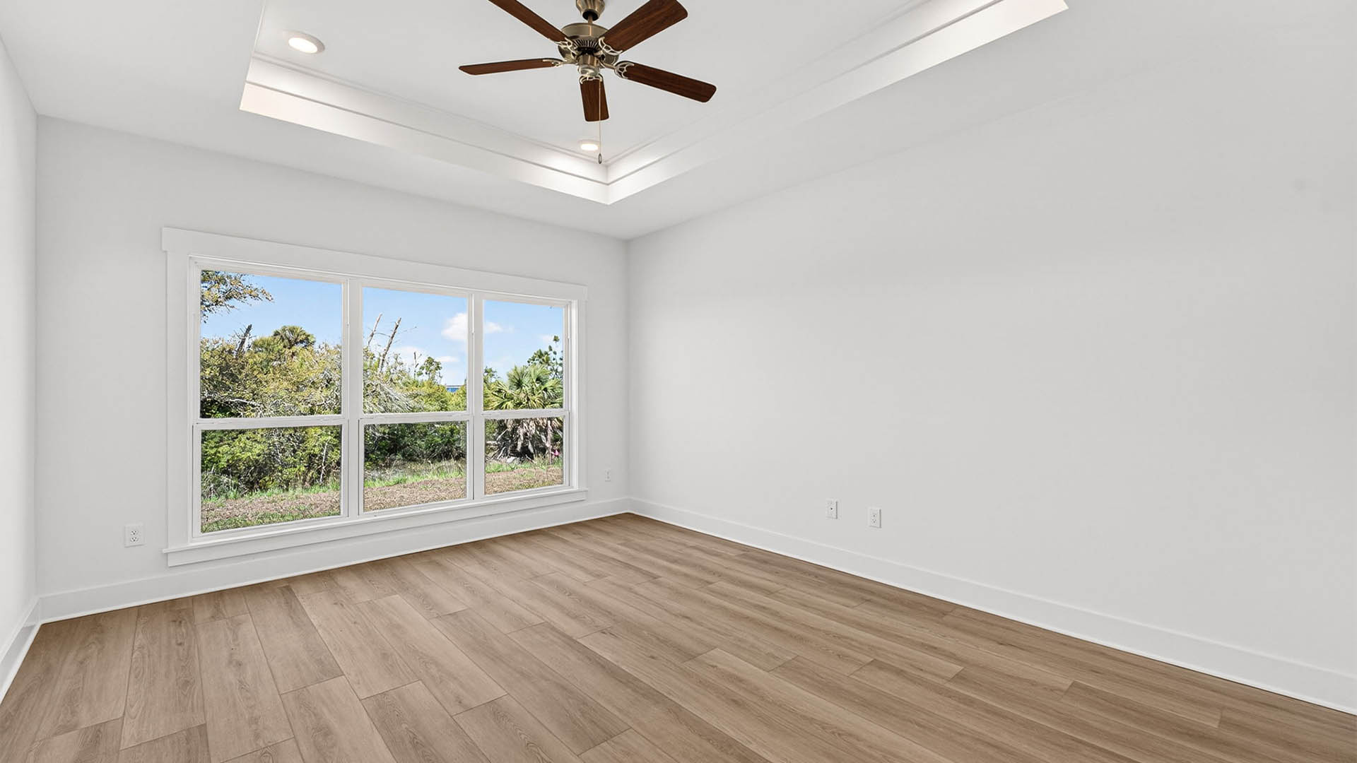 Primary bedroom with EVP flooring and ceiling fan and tray ceilings and window.