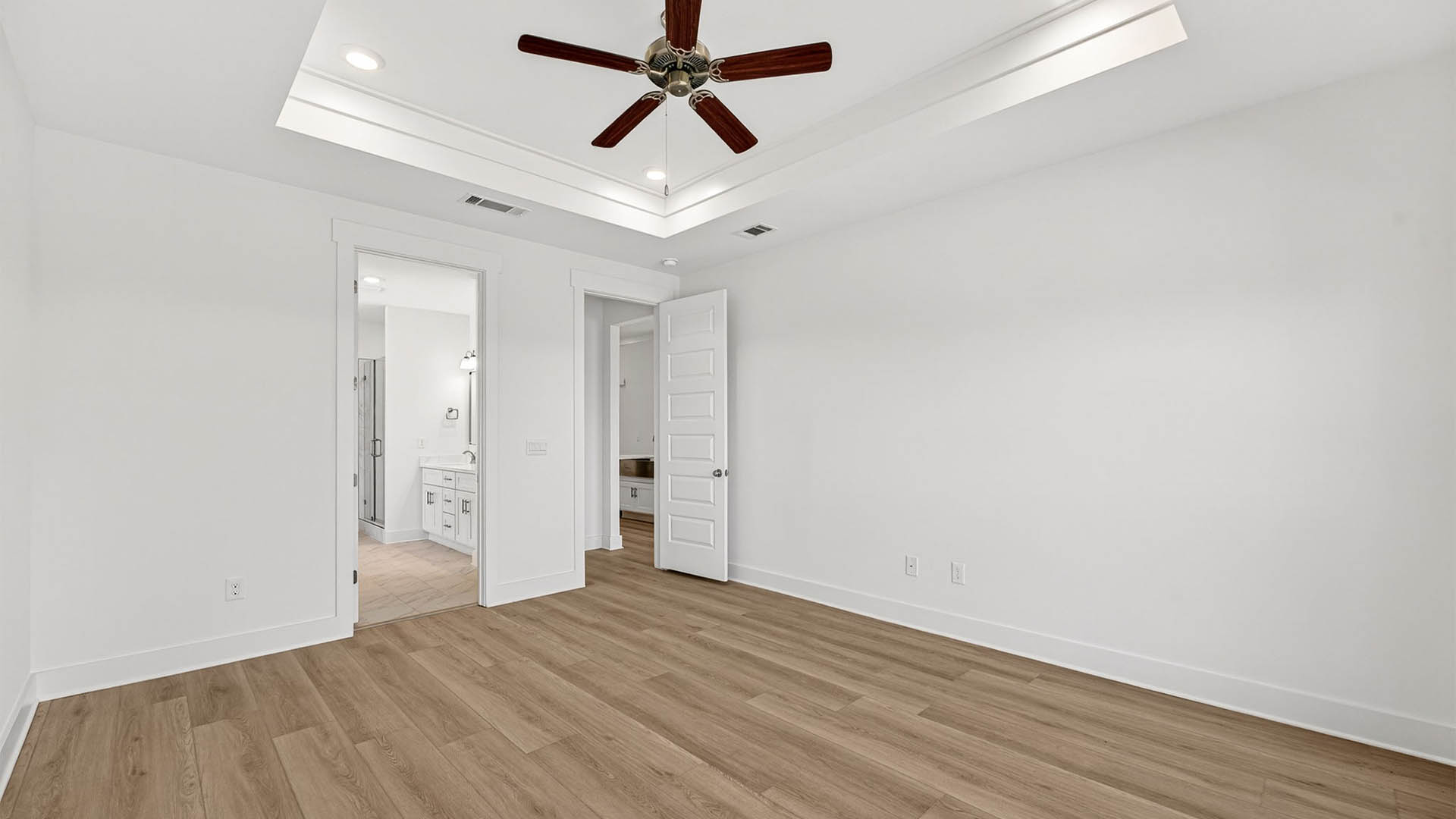 Primary bedroom with EVP flooring and ceiling fan and tray ceilings and bathroom entrance.