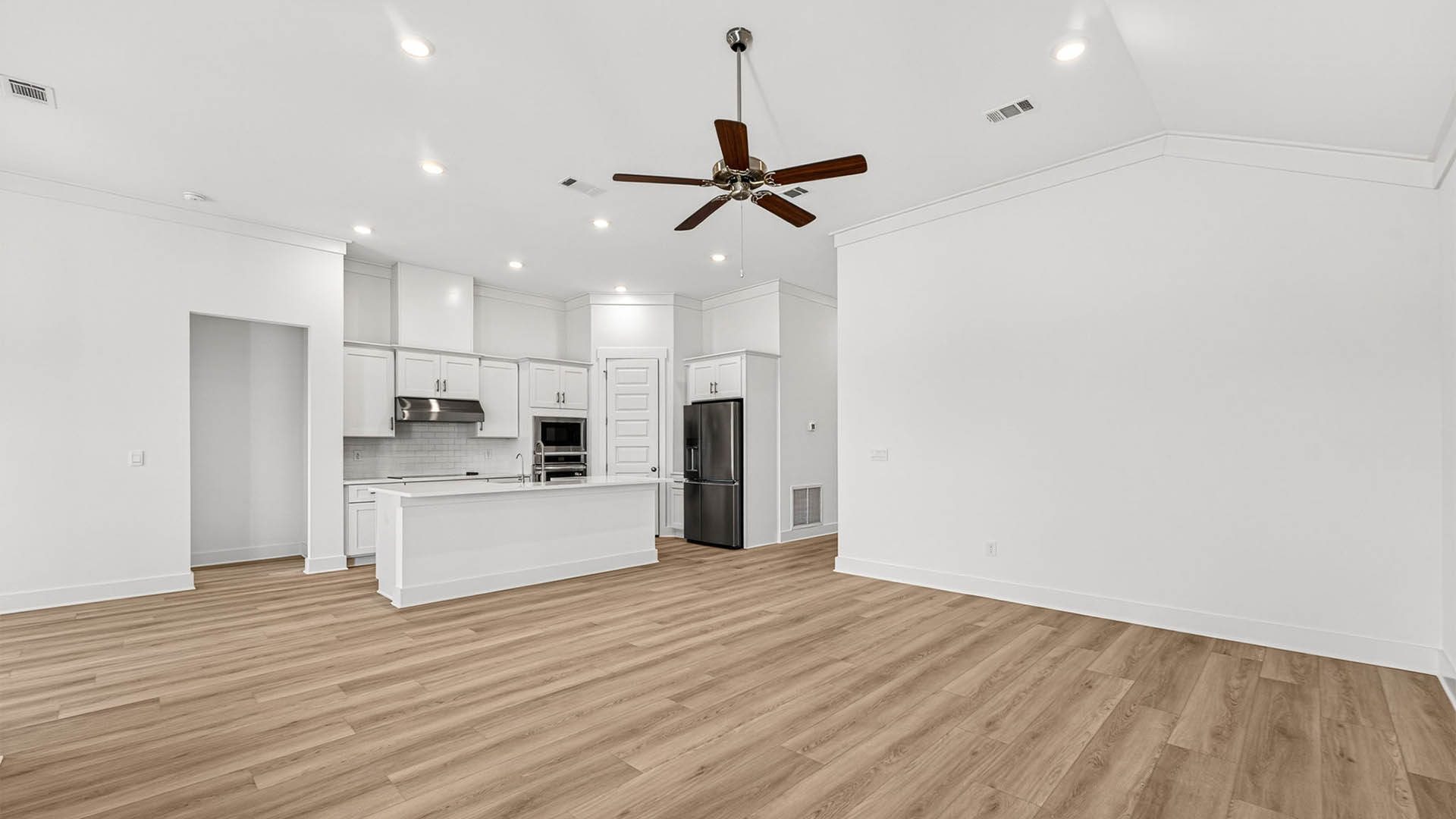 Open living room with ceiling fan and EVP flooring and kitchen.