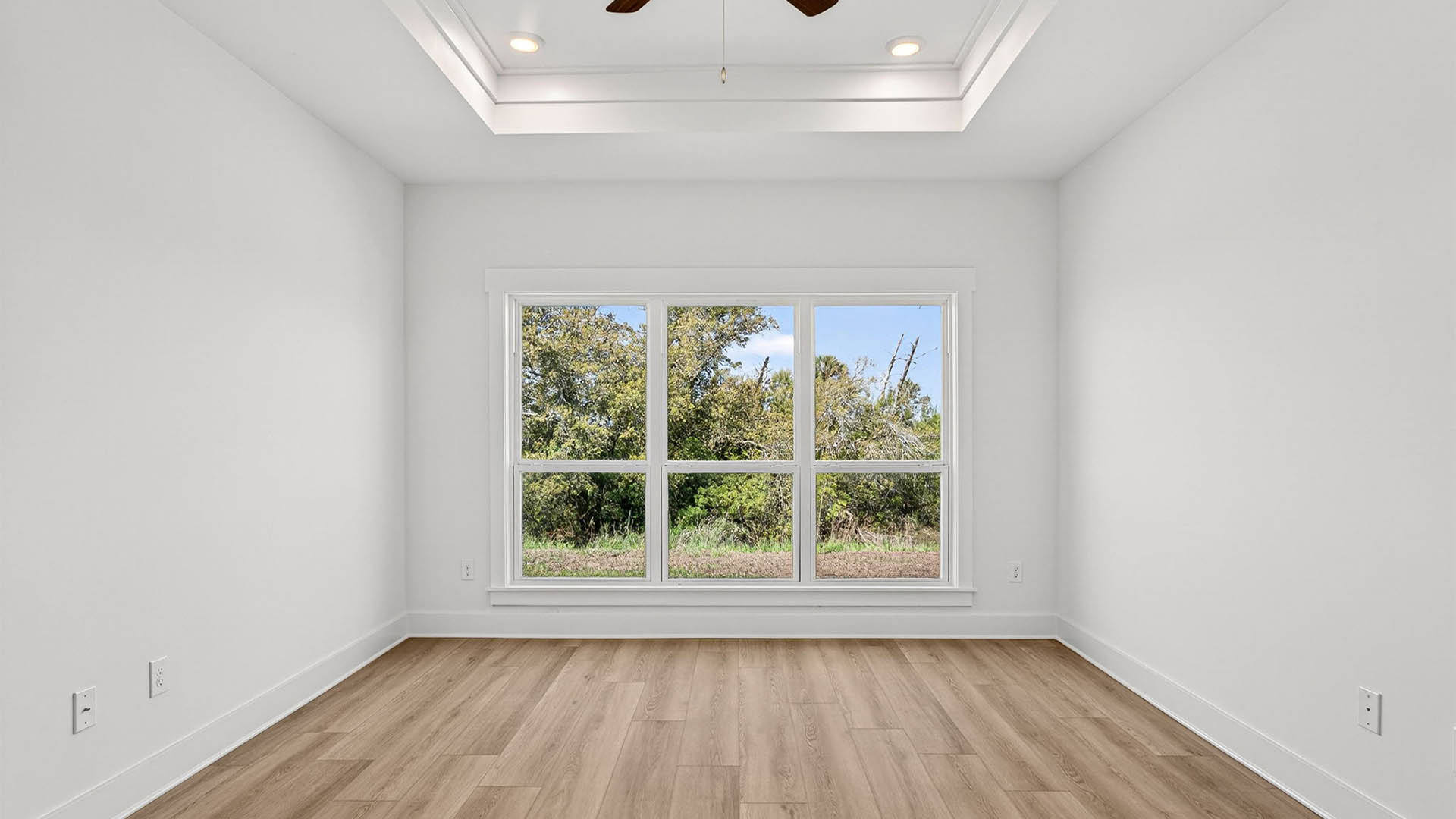 Primary bedroom with EVP flooring and ceiling fan and tray ceilings and window.