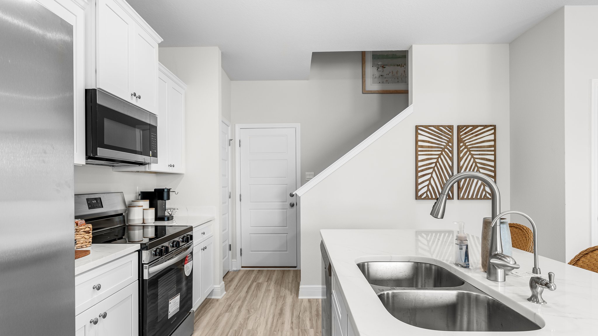 Kitchen with island and quartz countertops and stainless-steel appliances and white cabinets next to stairs and garage.