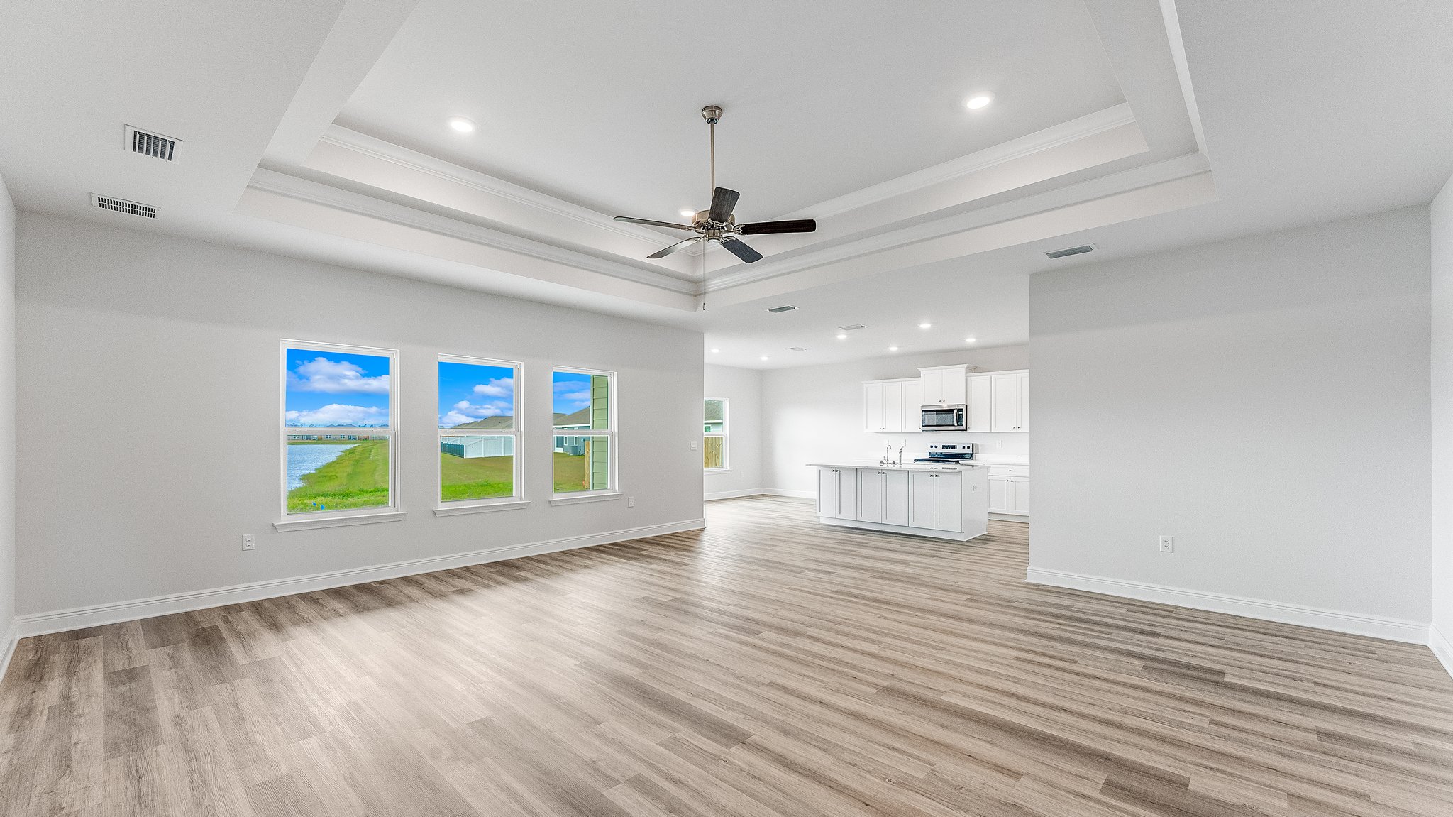 Open living room with EVP flooring and tray ceilings and ceiling fan and 3 windows and kitchen.
