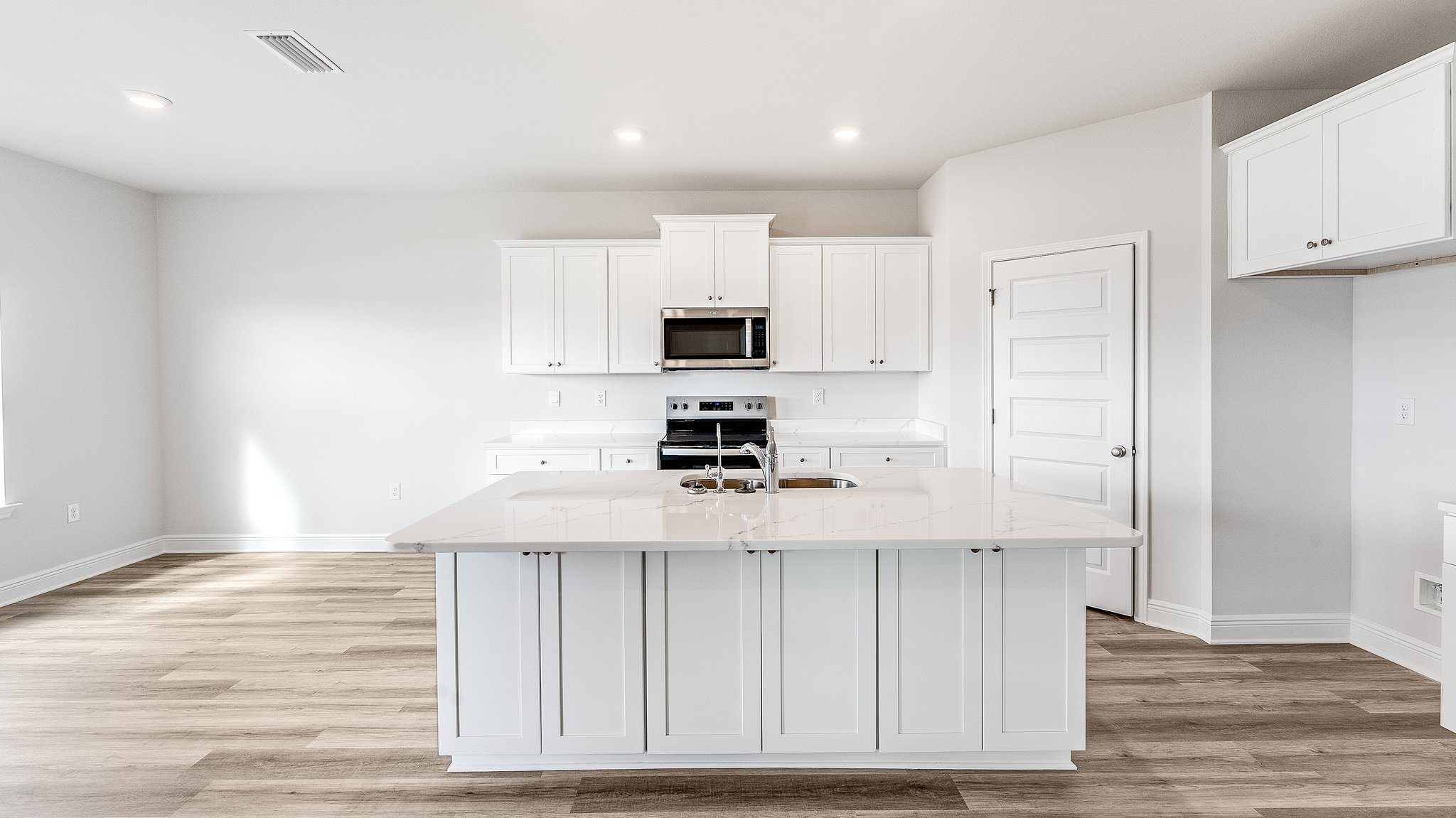 Kitchen with island with white cabinets and quartz countertops and pantry and stainless-steel appliances.