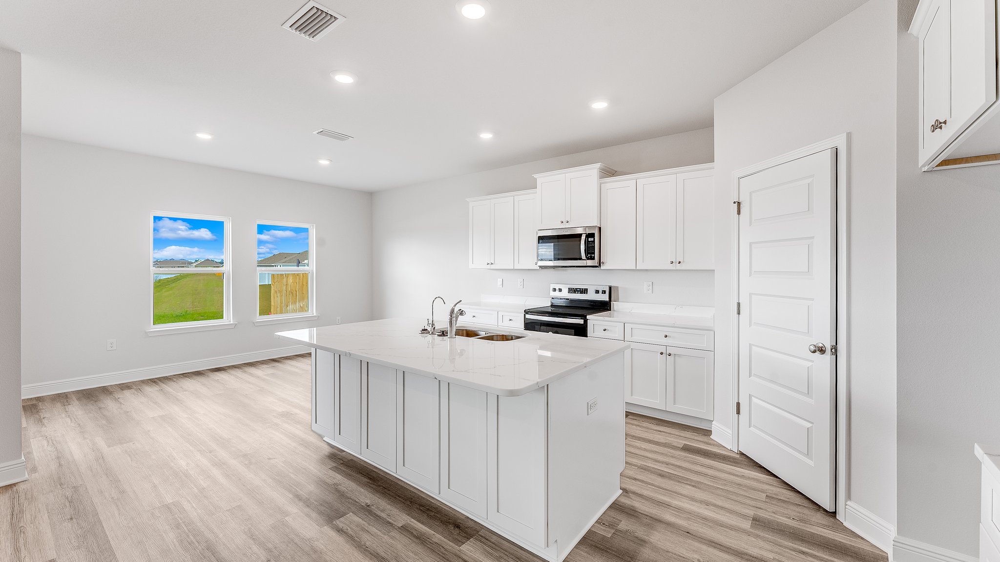 Kitchen with island with white cabinets and quartz countertops and pantry and stainless-steel appliances.
