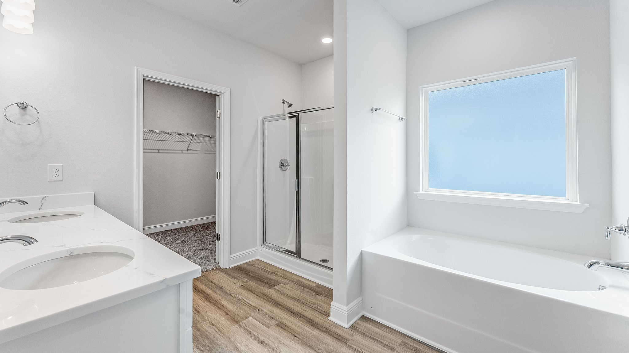 Primary bathroom with EVP flooring and white cabinets and double vanity with quartz countertops and walk-in shower with glass doors and tub with window and closet.