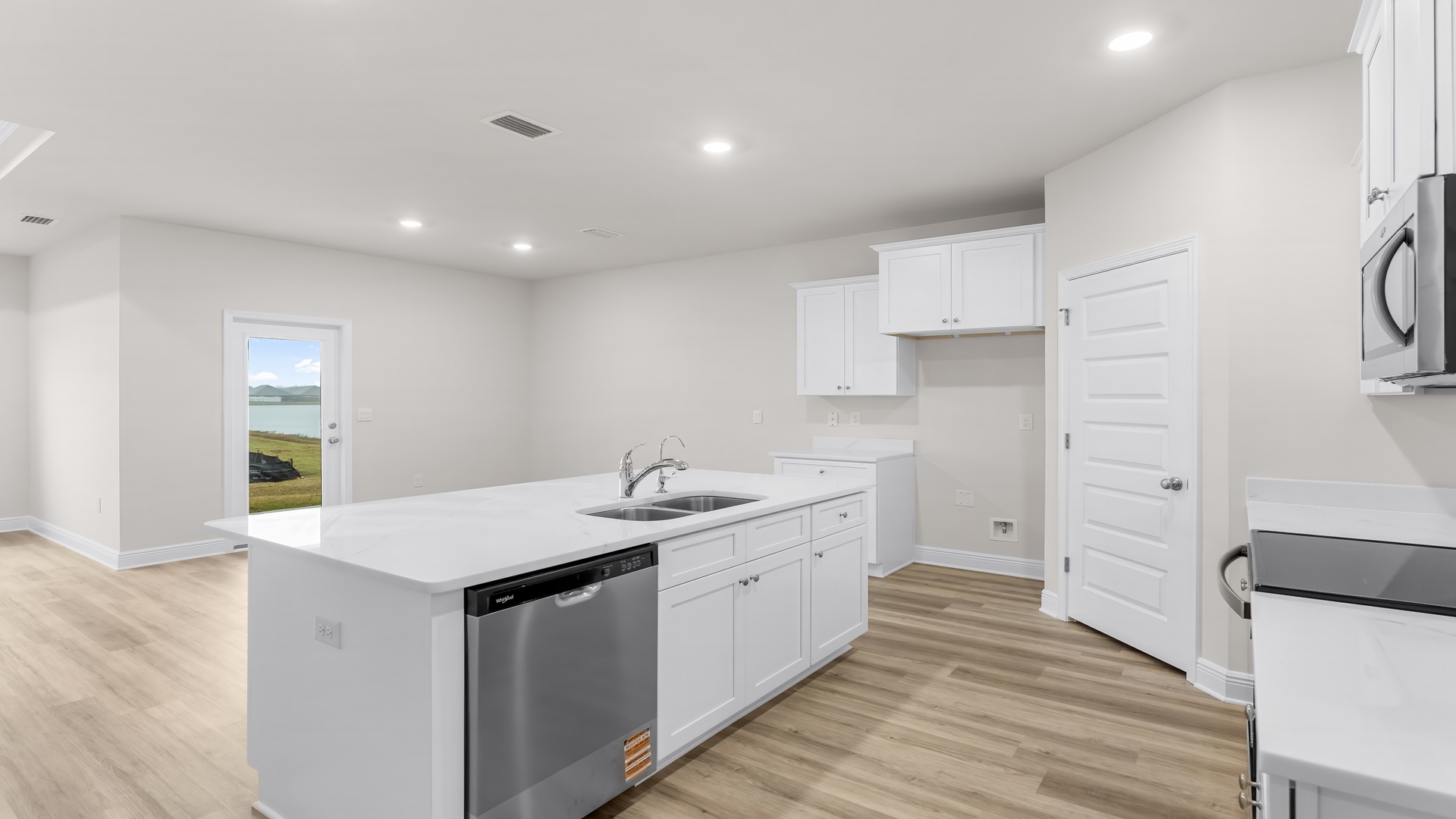 Kitchen with large island with white cabinets and quartz countertops and stainless-steel appliances and walk-in pantry.