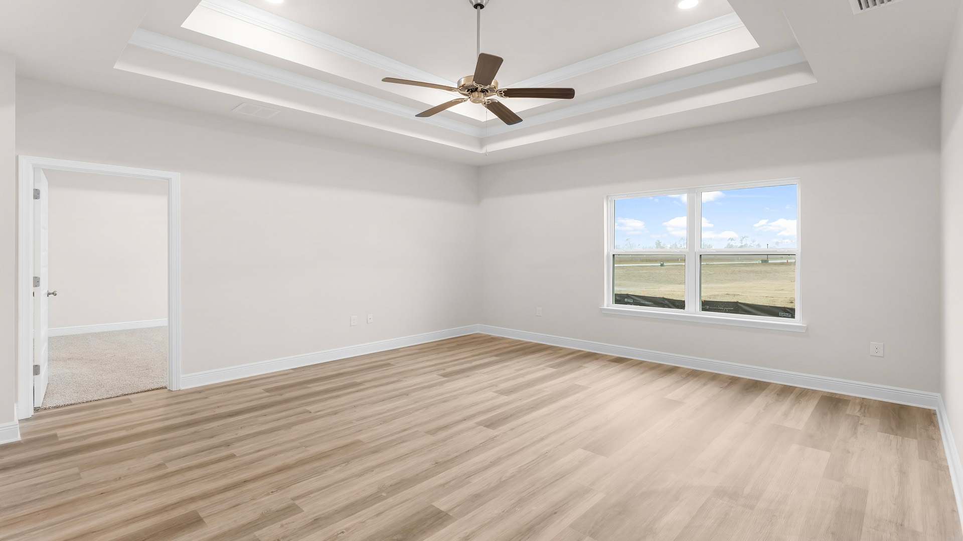 Open living room with tray ceilings and ceiling fan and EVP flooring and large windows.