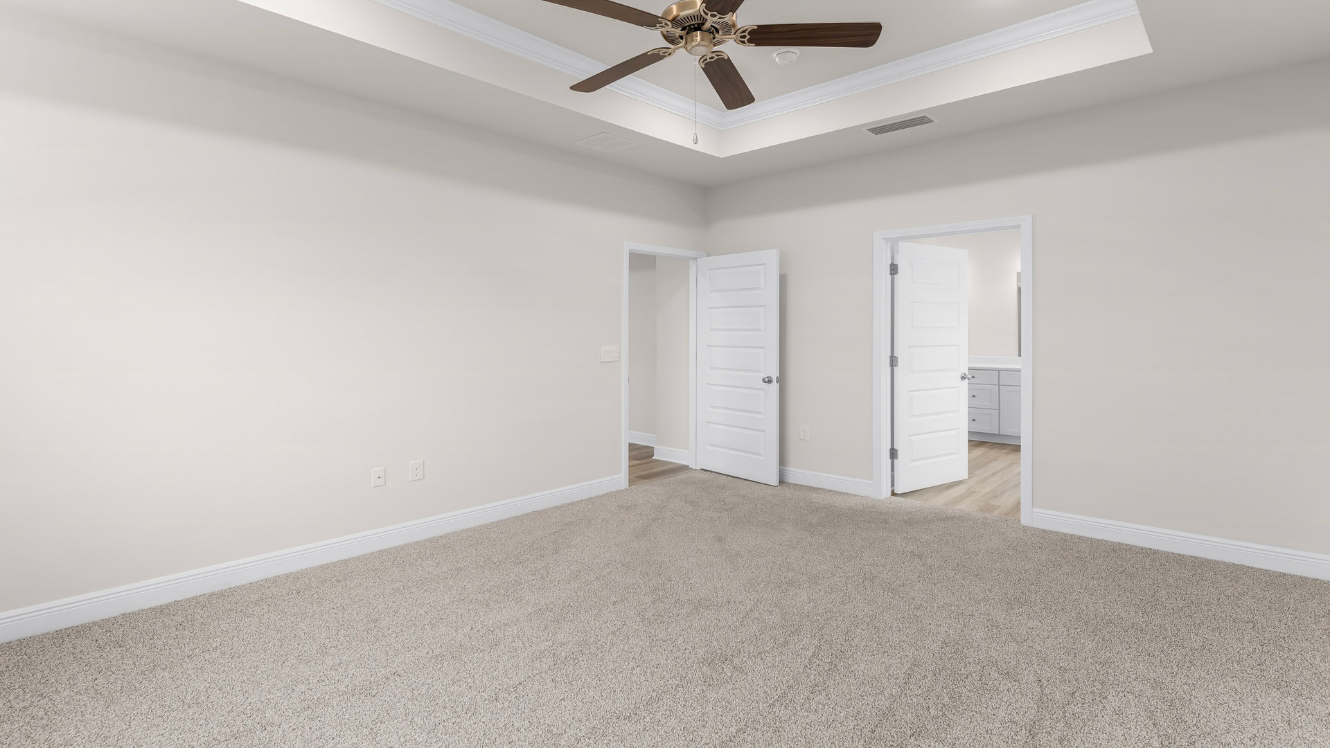 Primary bedroom with carpet floors and tray ceilings and ceiling fan and primary bathroom entrance.