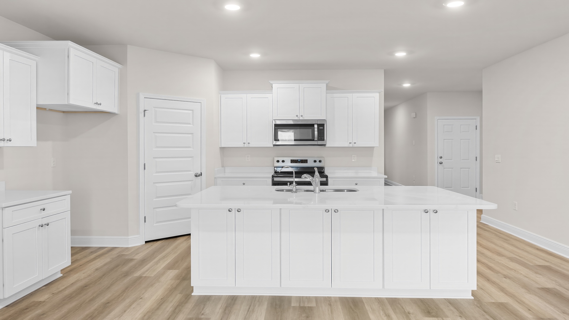Kitchen with large island with white cabinets and quartz countertops and stainless-steel appliances and walk-in pantry.