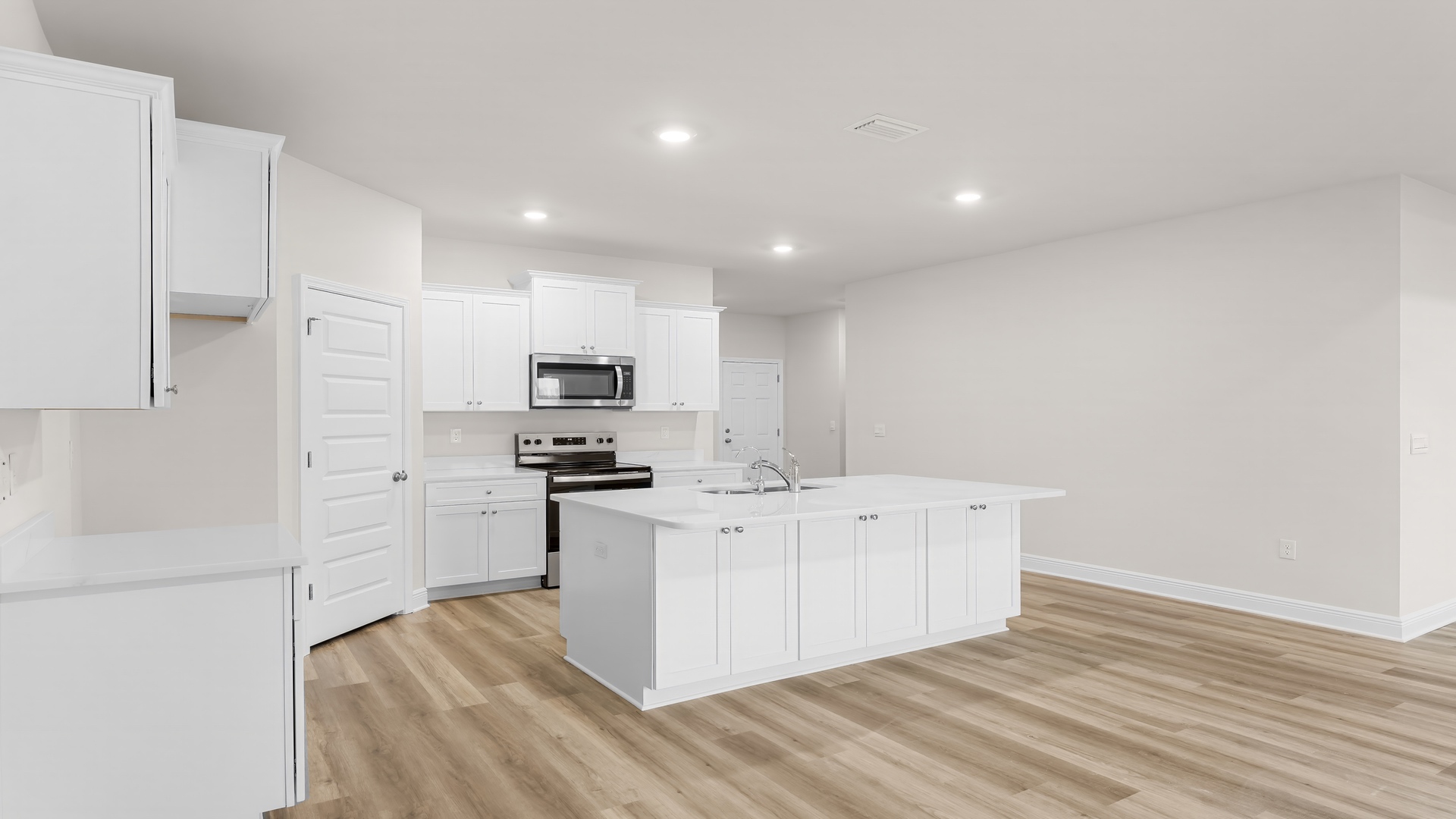 Kitchen with large island with white cabinets and quartz countertops and stainless-steel appliances and walk-in pantry.