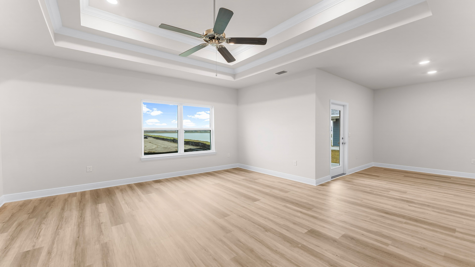 Open living room with tray ceilings and ceiling fan and EVP flooring and large windows.