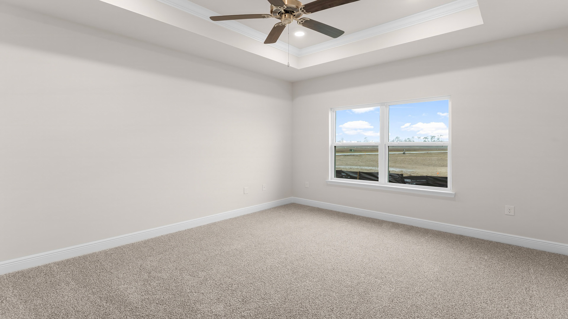 Primary bedroom with carpet floors and tray ceilings and ceiling fan and large windows.