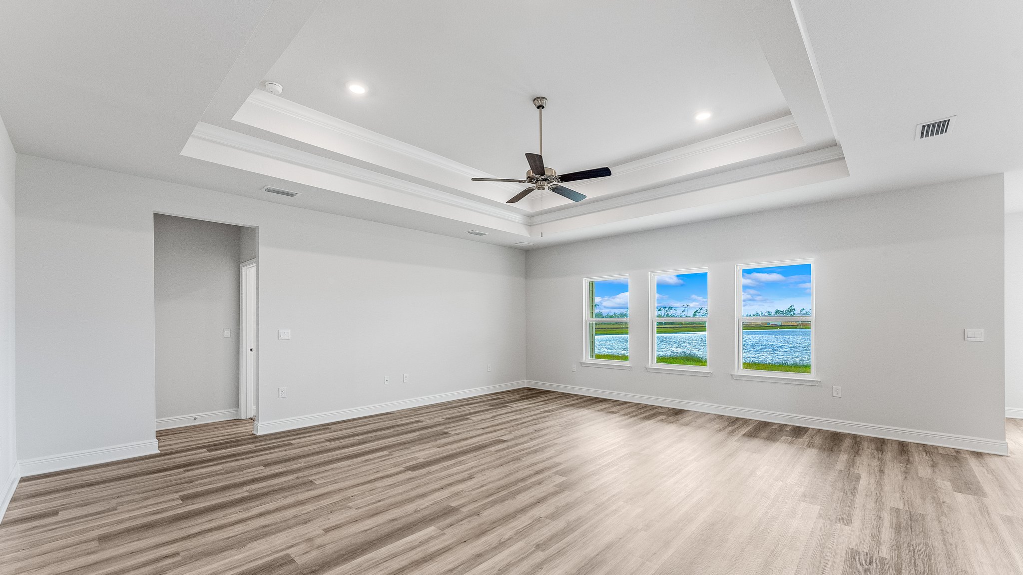 Open living room with EVP flooring and tray ceilings and ceiling fan and 3 windows.