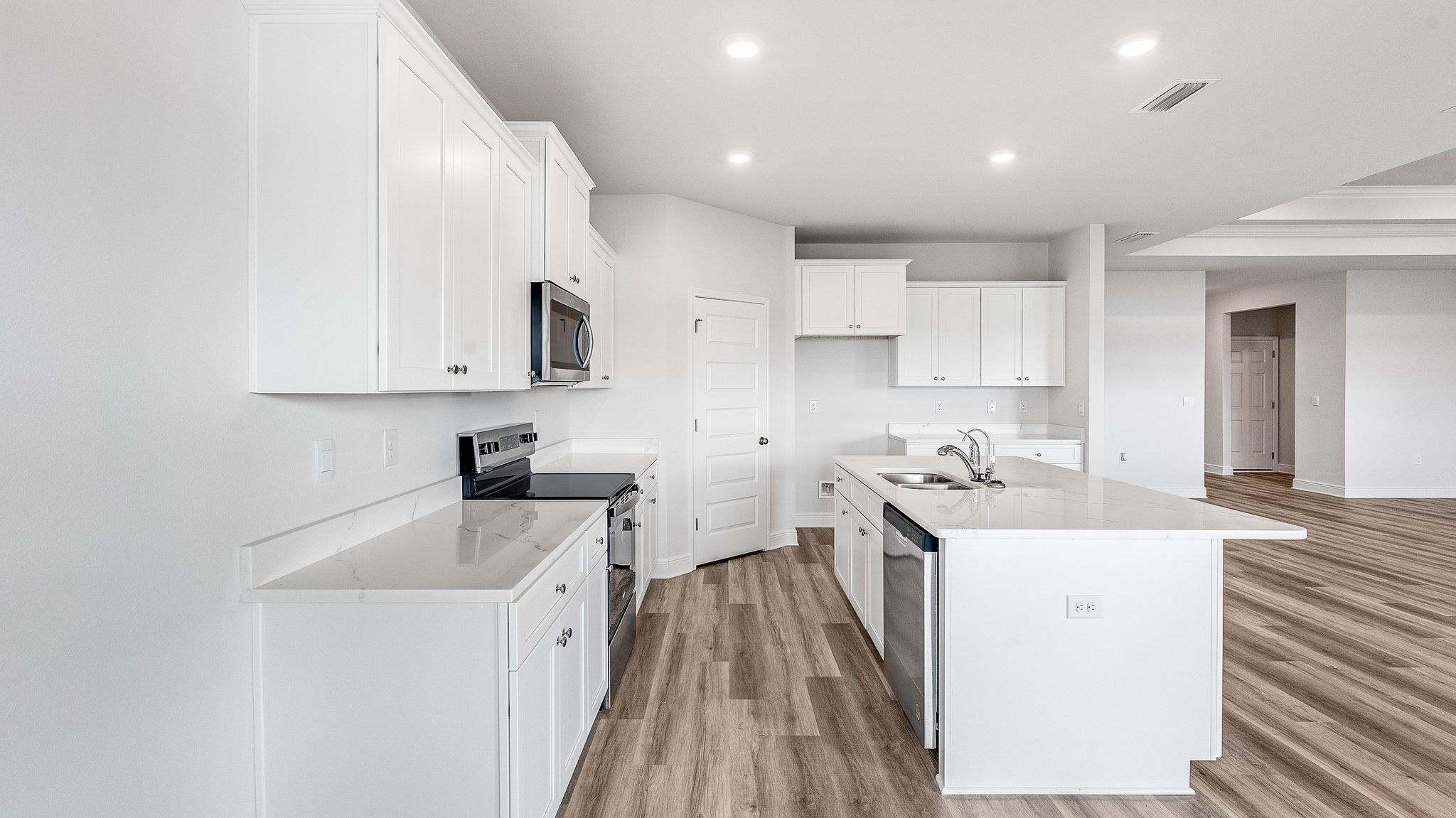 Kitchen with island with white cabinets and quartz countertops and pantry and stainless-steel appliances.