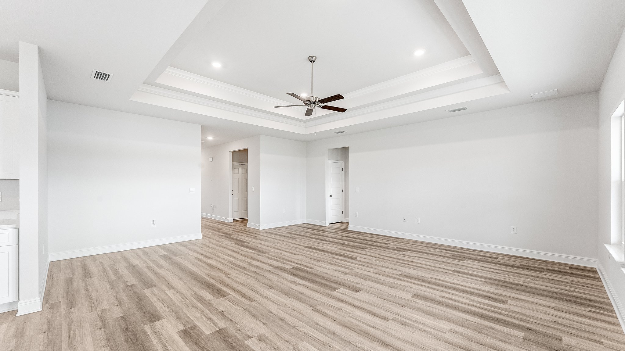 Open living room with EVP flooring and tray ceilings and ceiling fan.