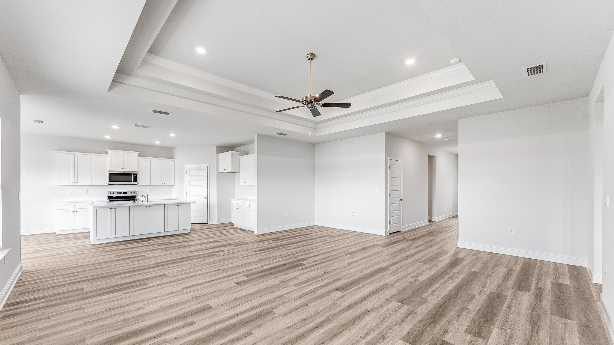 Open living room with EVP flooring and tray ceilings and ceiling fan and 3 windows and kitchen.