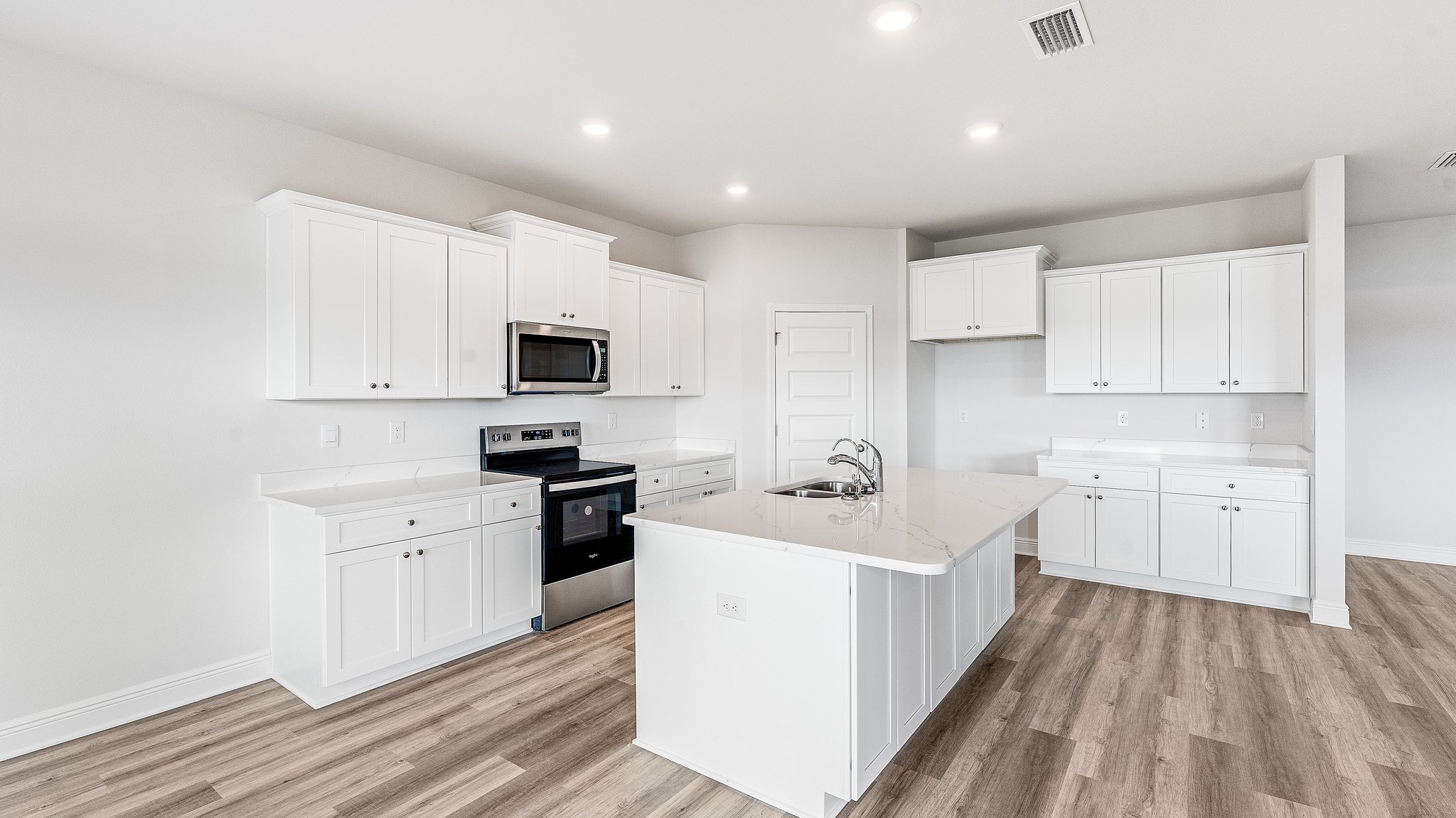 Kitchen with island with white cabinets and quartz countertops and pantry and stainless-steel appliances.