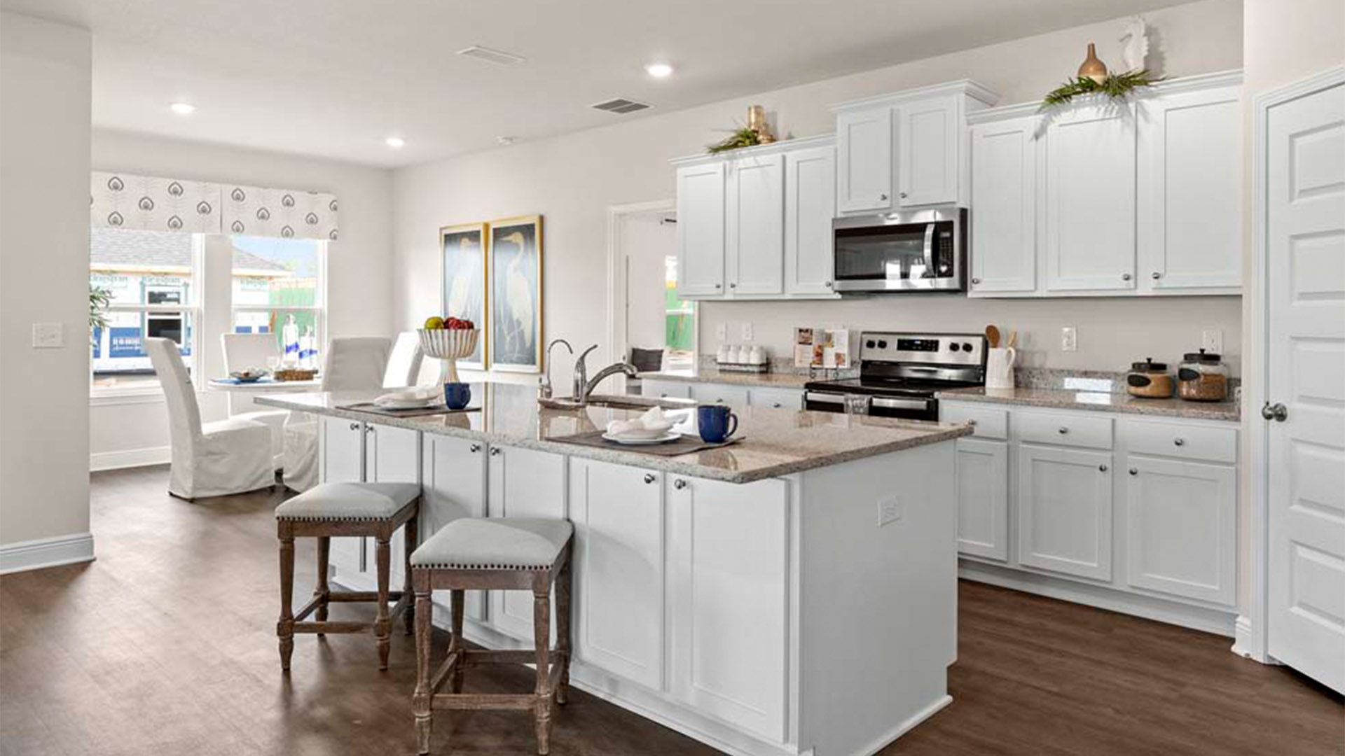 Open kitchen with island with granite countertops and stainless-steel appliances and white cabinets and pantry.