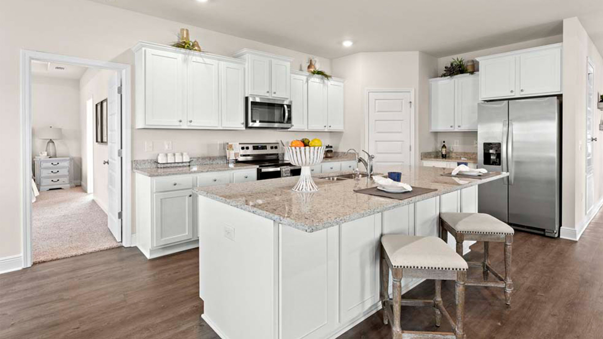 Open kitchen with island with granite countertops and stainless-steel appliances and white cabinets and pantry.