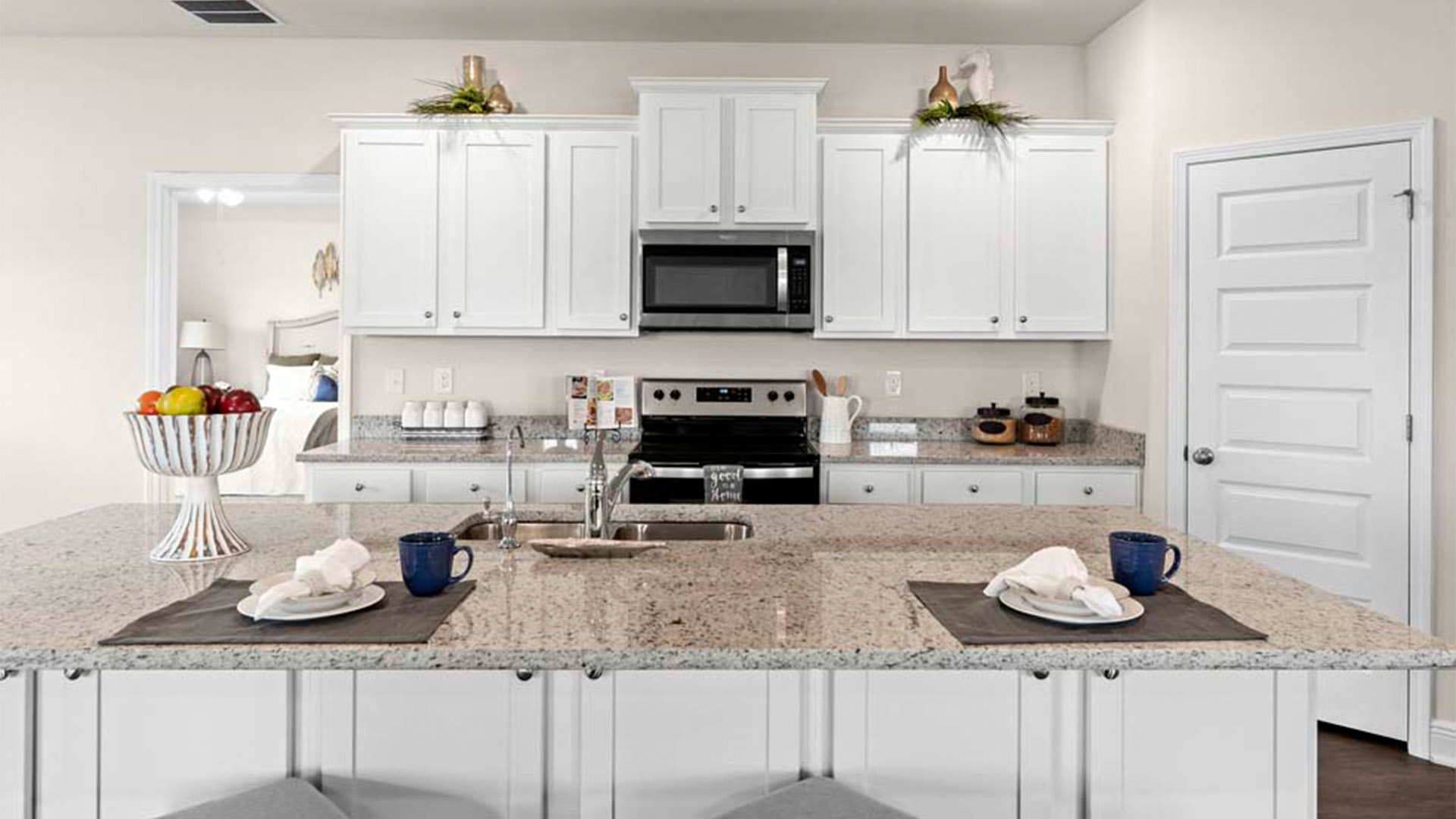 Open kitchen with island with granite countertops and stainless-steel appliances and white cabinets and pantry.