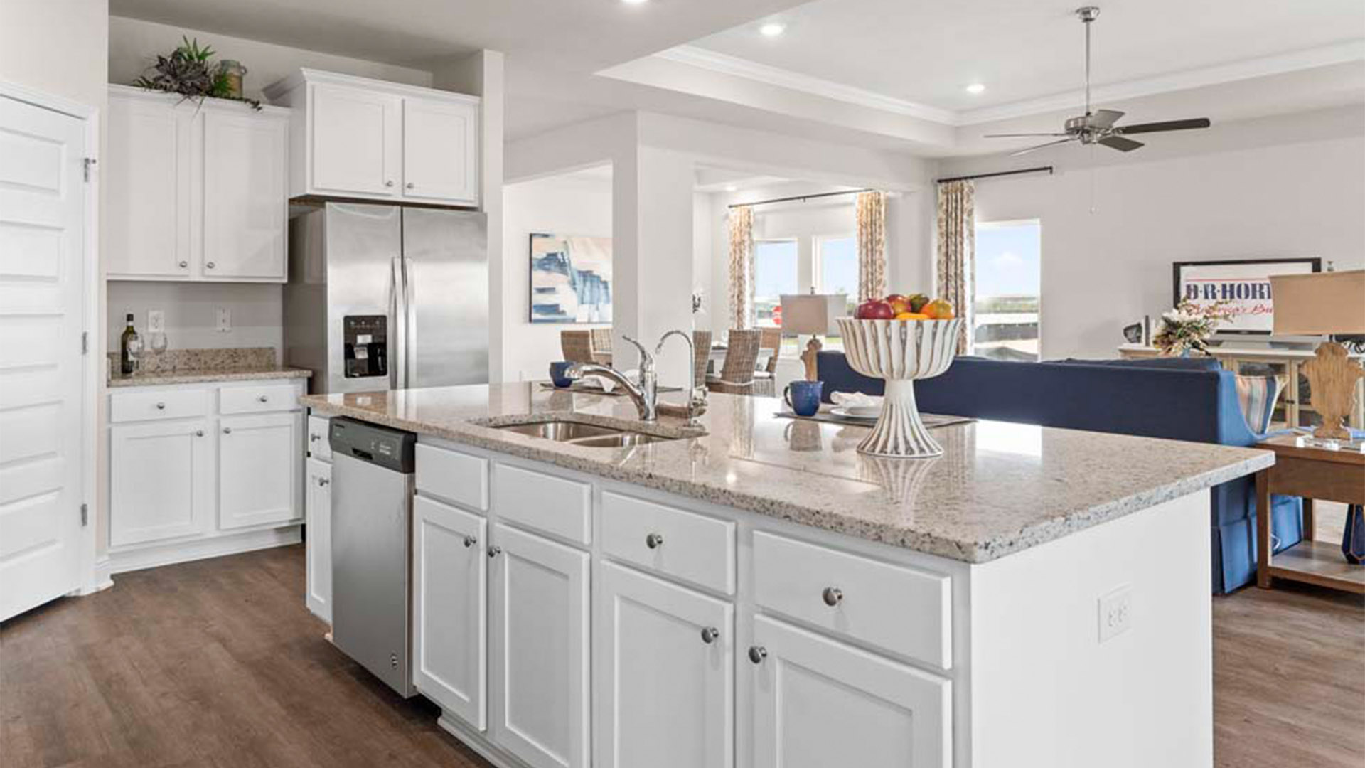 Open kitchen with island with granite countertops and stainless-steel appliances and white cabinets and pantry.