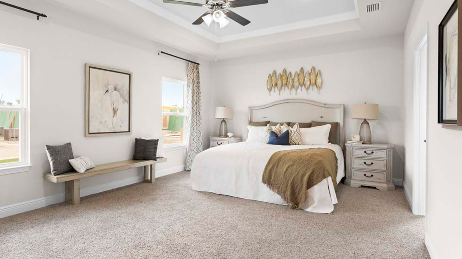 Primary bedroom with carpet floors and ceiling fan and tray ceilings and windows.