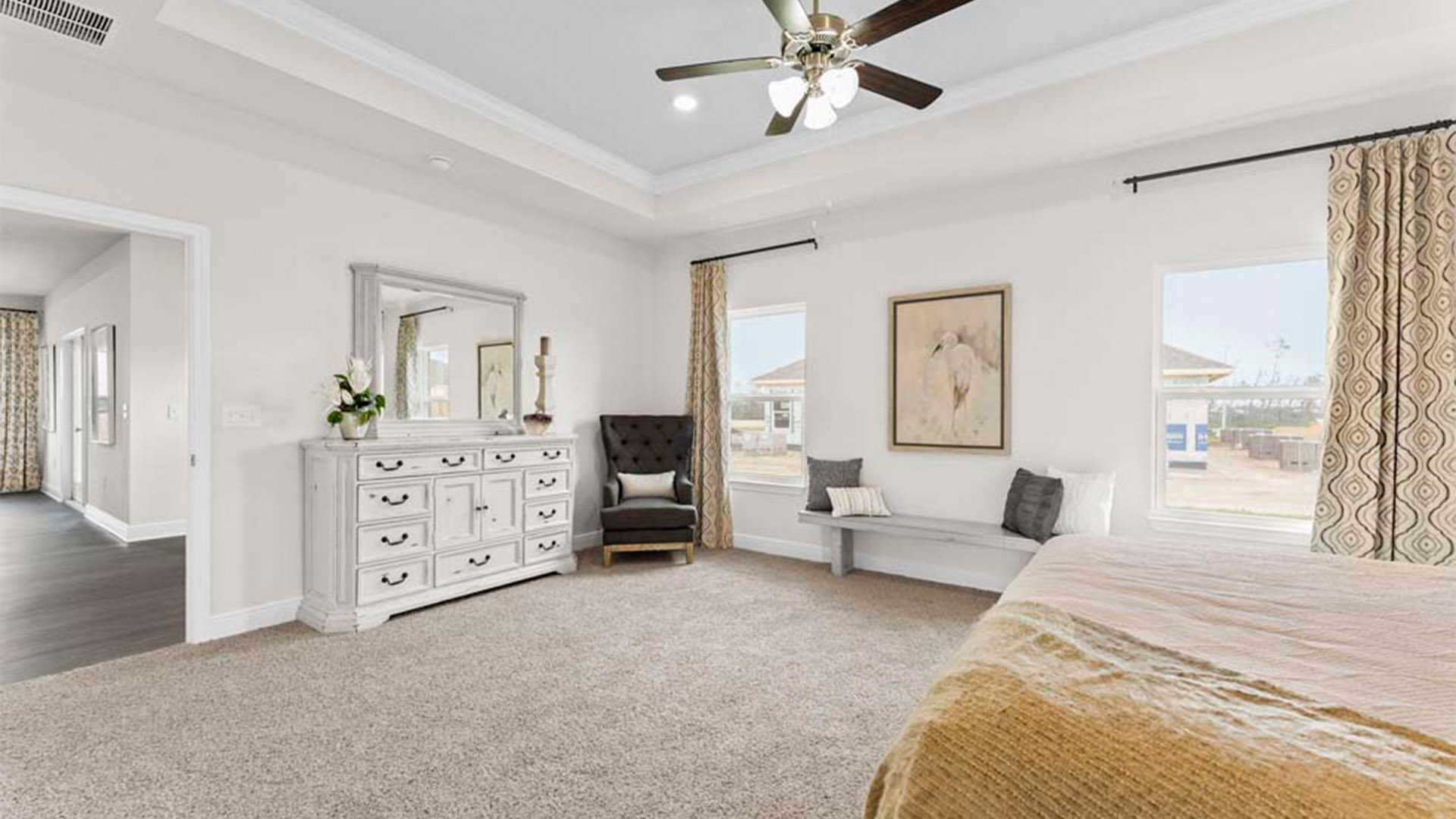 Primary bedroom with carpet floors and ceiling fan and tray ceilings and windows.