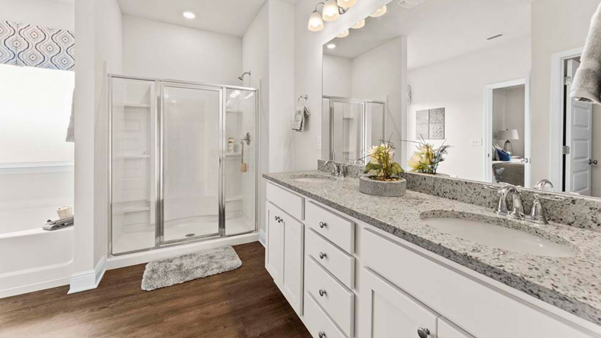 Primary bathroom with granite countertops and double vanity and white cabinets and tub and shower with glass doors.