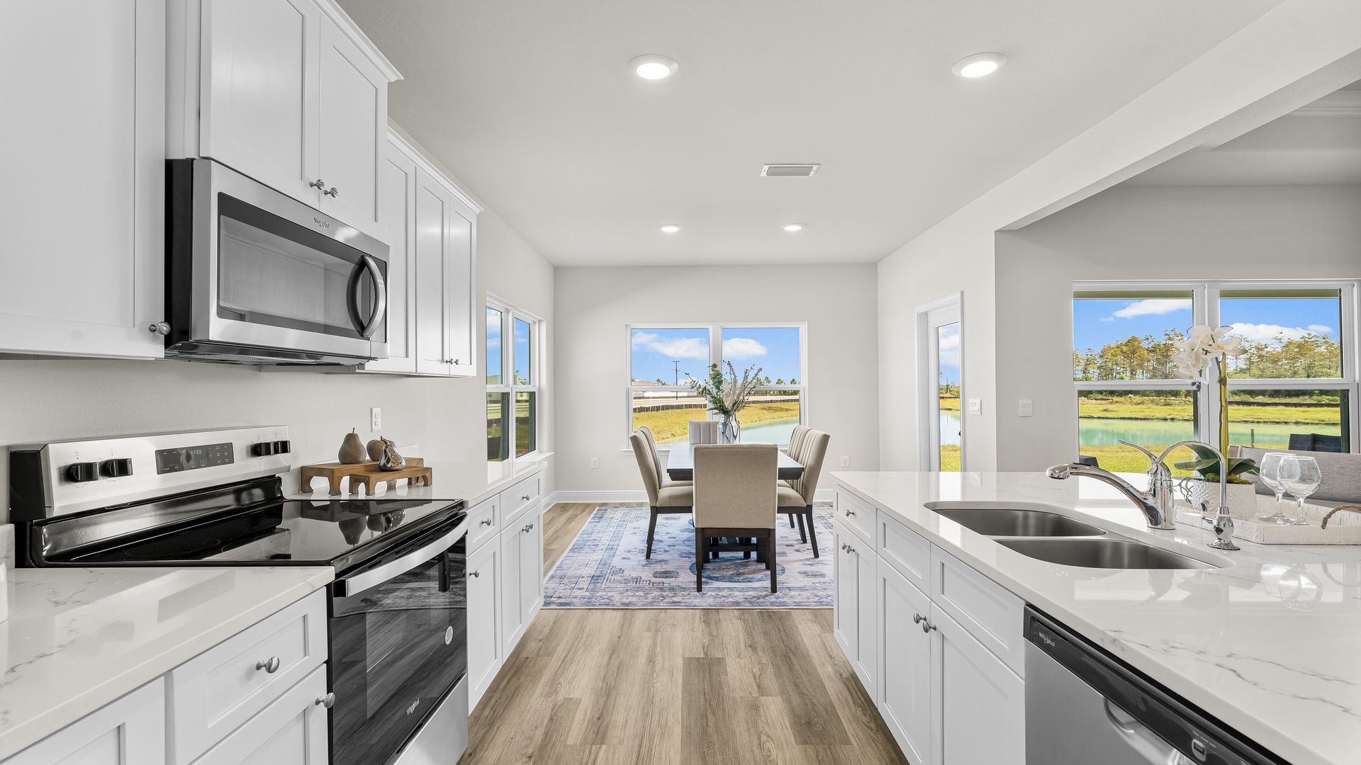 Open kitchen with island with quartz countertops and white cabinets and stainless-steel appliances and dining area next to back door.