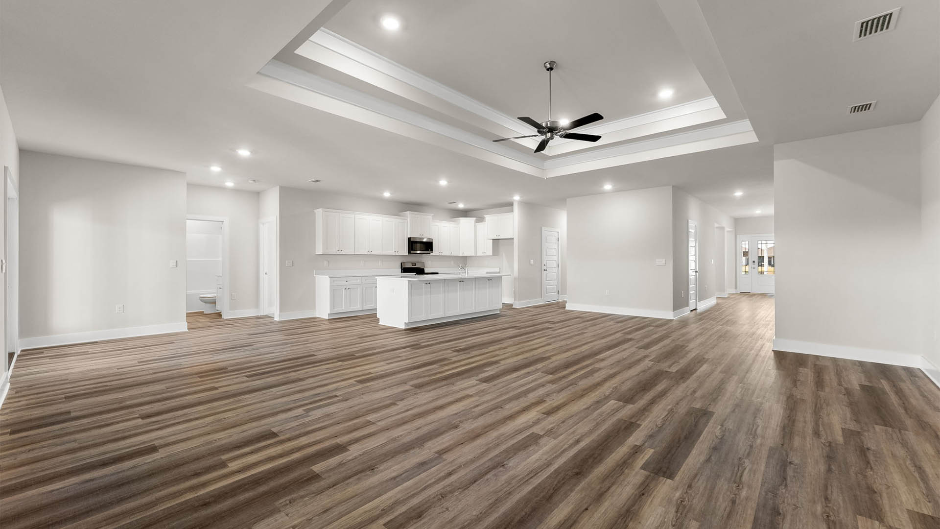 Open living room with EVP flooring and tray ceilings and ceiling fan.