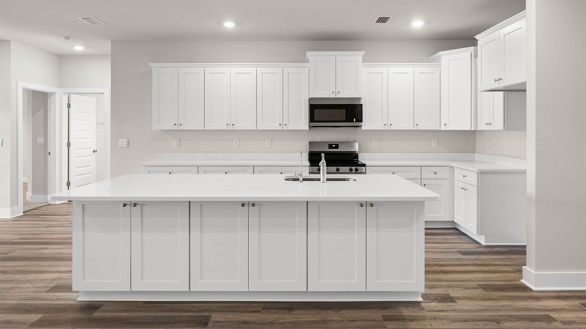 Open kitchen with island with quartz countertops and stainless-steel appliances and white cabinets.