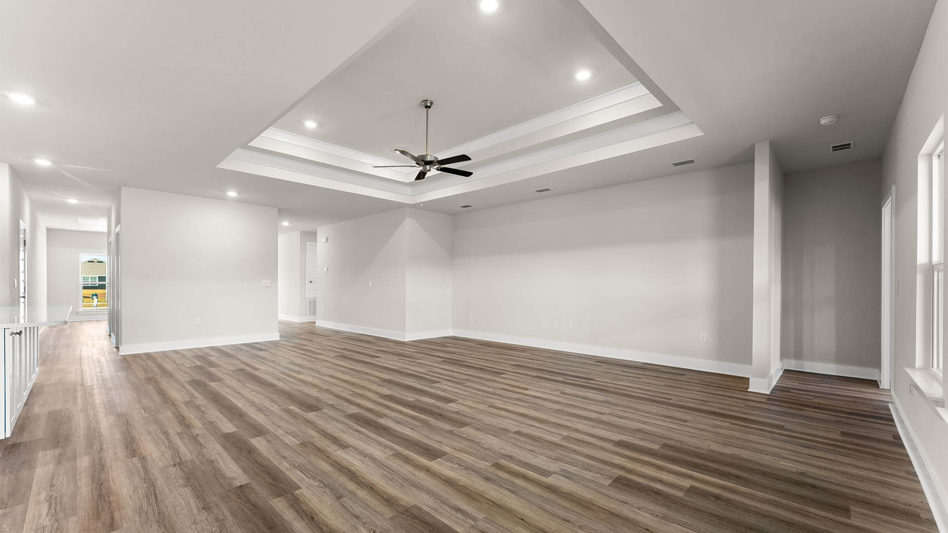Open living room with EVP flooring and tray ceilings and ceiling fan.