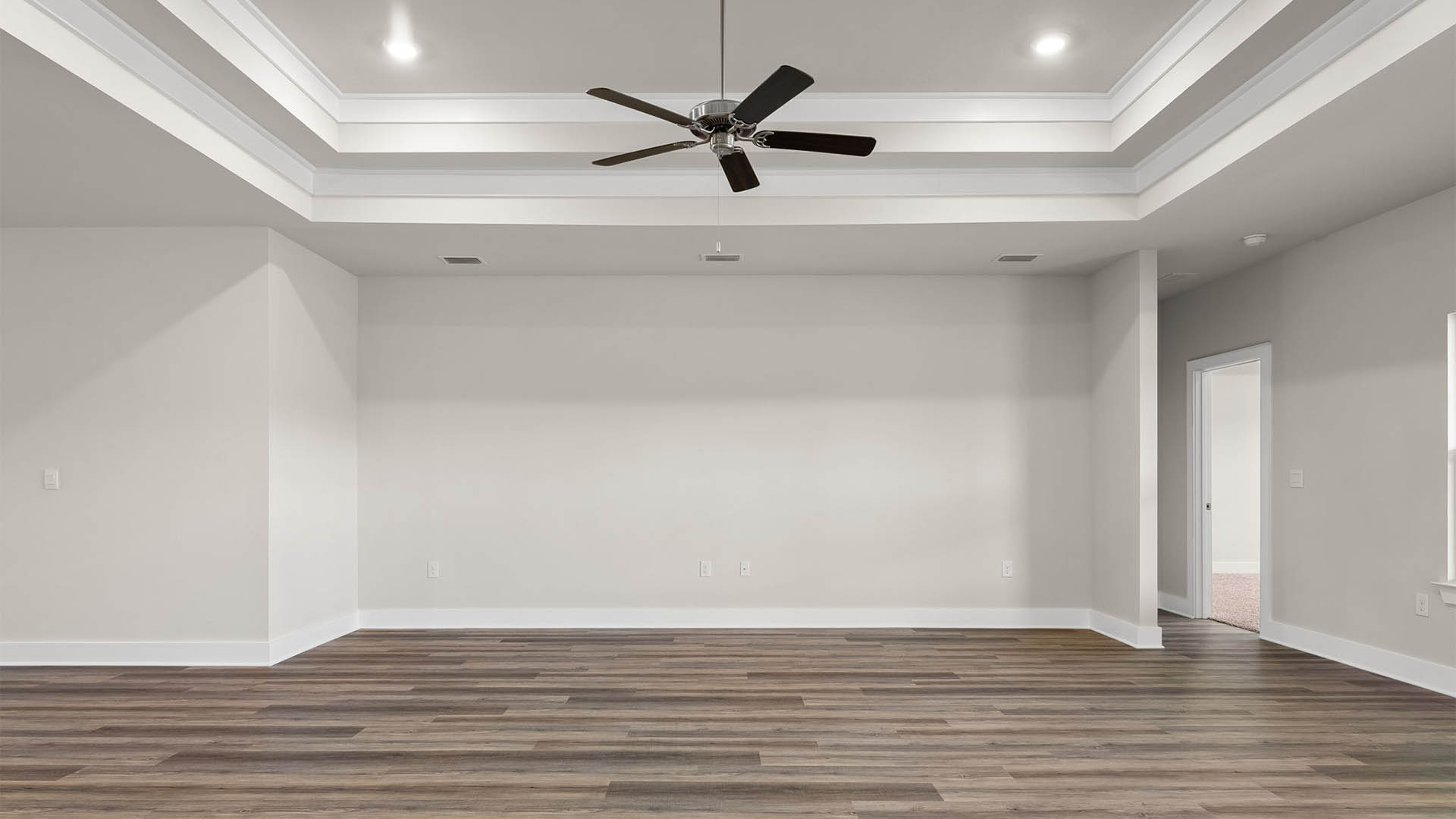 Open living room with EVP flooring and tray ceilings and ceiling fan.