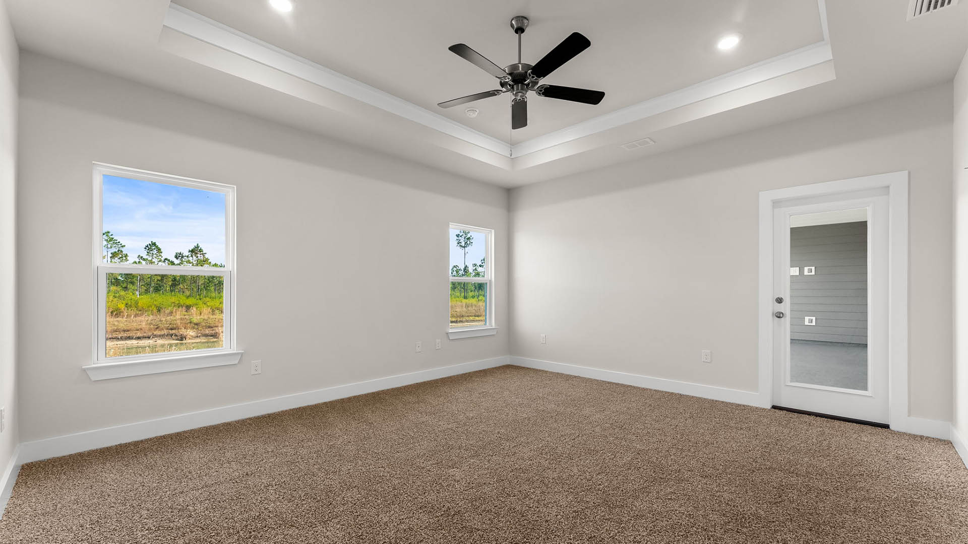 Primary bedroom with carpet floors and ceiling fan and tray ceilings and windows and patio door.