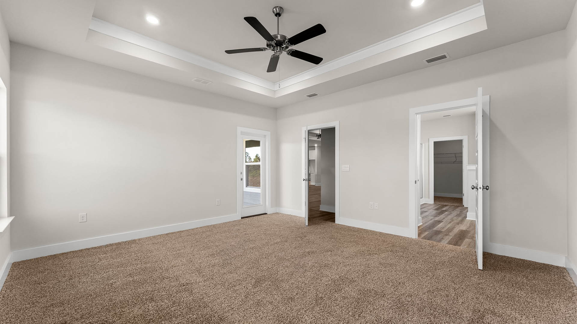 Primary bedroom with carpet floors and ceiling fan and tray ceilings and bathroom entrance and patio door.