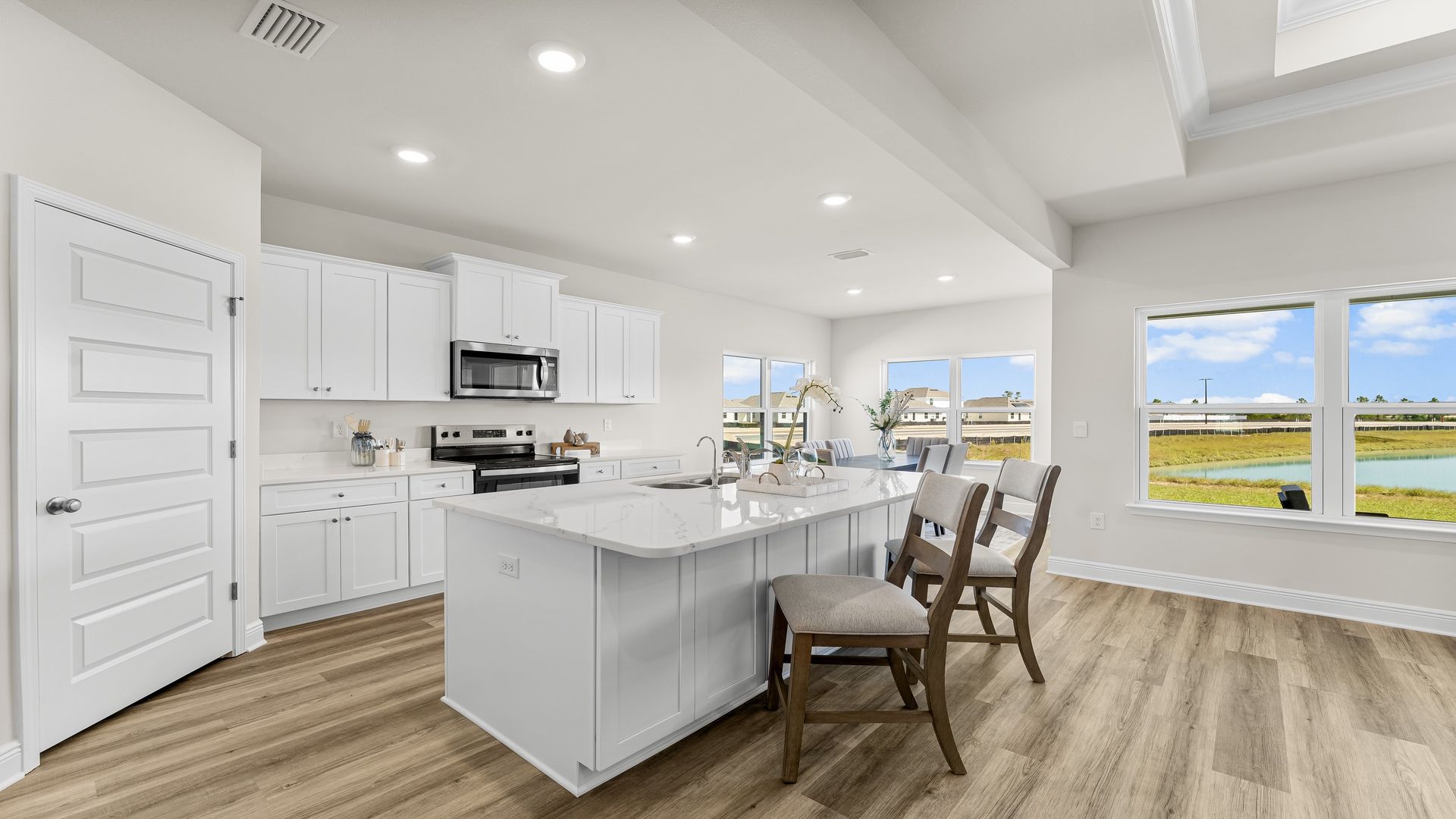 Open kitchen with island with quartz countertops and white cabinets and stainless-steel appliances and pantry.