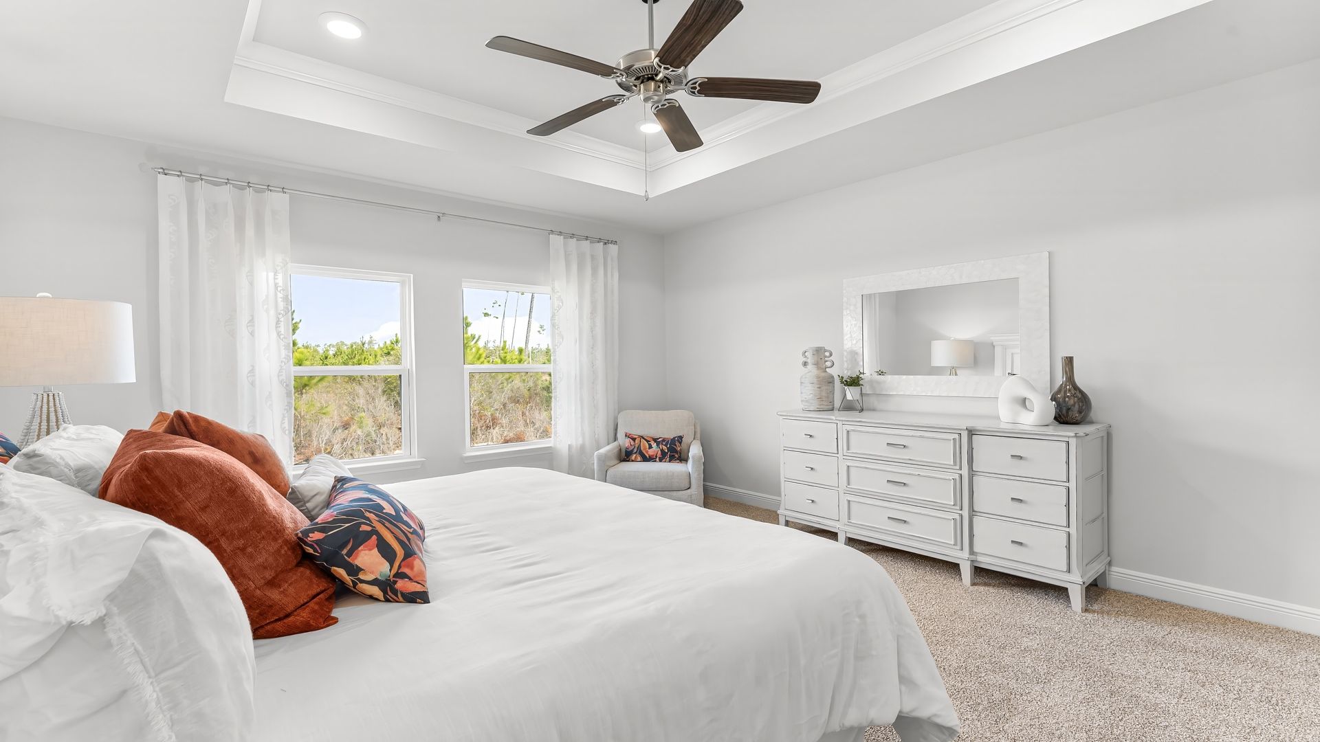 Primary bedroom with carpet floors and ceiling fan and tray ceilings and two windows.