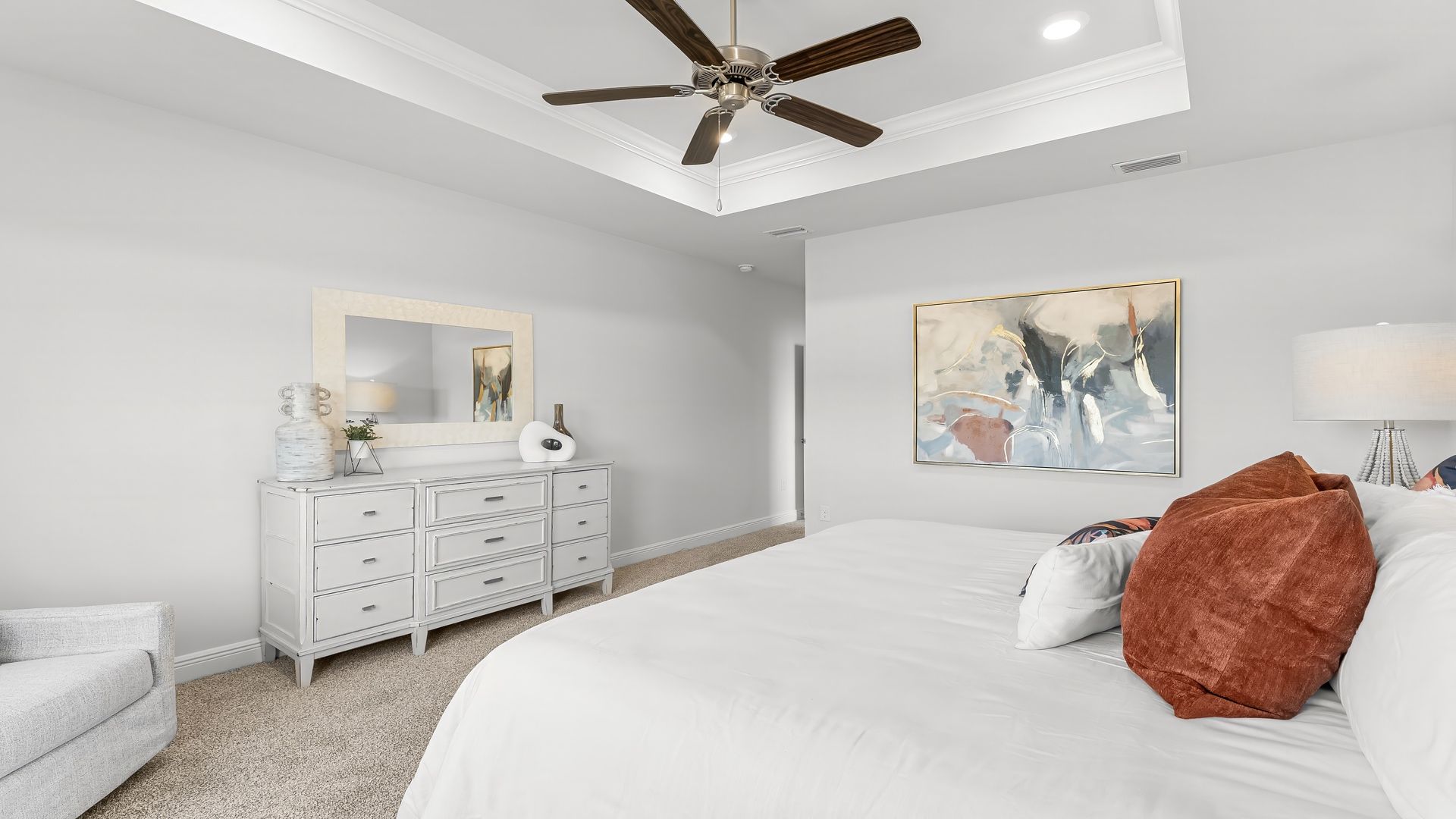 Primary bedroom with carpet floors and ceiling fan and tray ceilings.