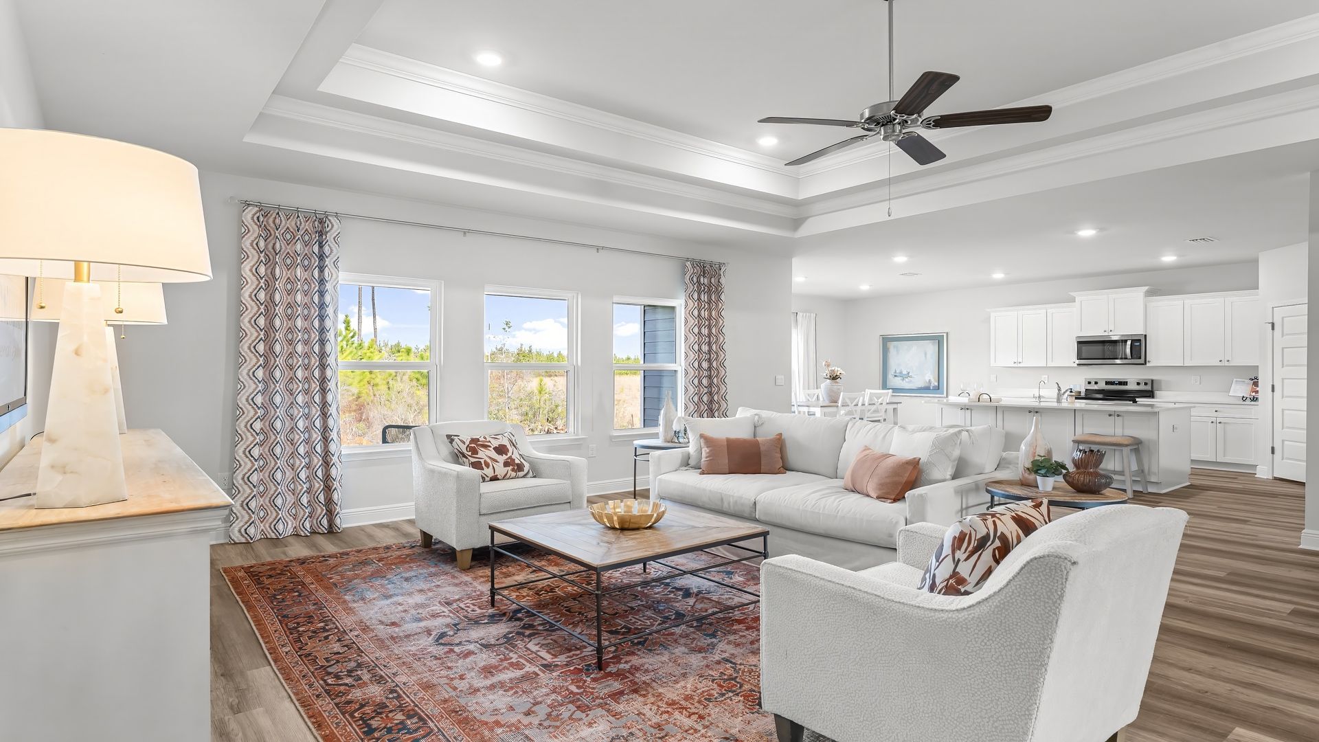 Open living room with EVP flooring and tray ceilings and ceiling fan and 3 windows.