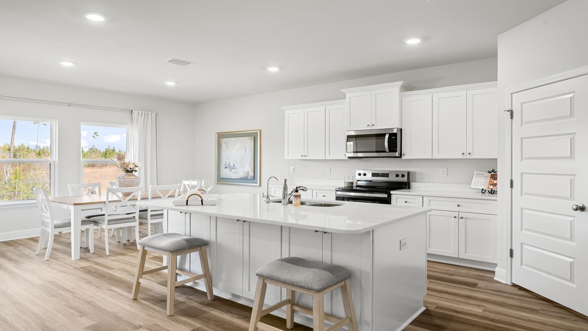Kitchen with island with white cabinets and quartz countertops and pantry and stainless-steel appliances.